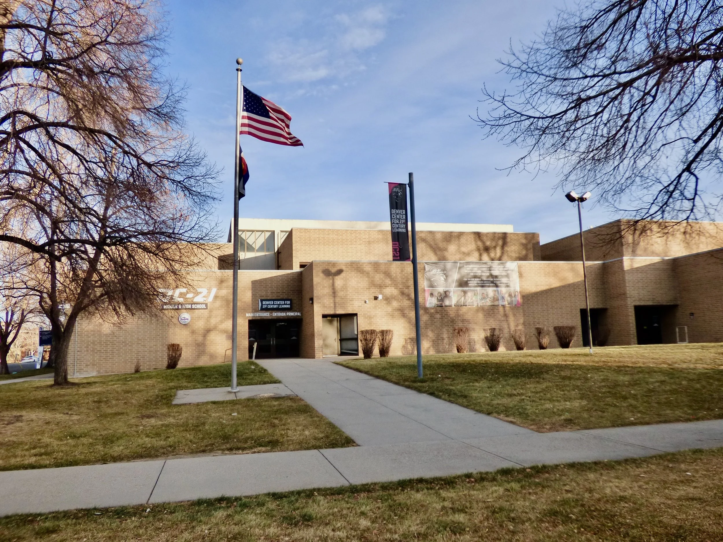 The Denver Center for K-12 Centennial High School building with an American flag flying in front on a clear day at Denver Century of 21st Learning, Denver, CO.