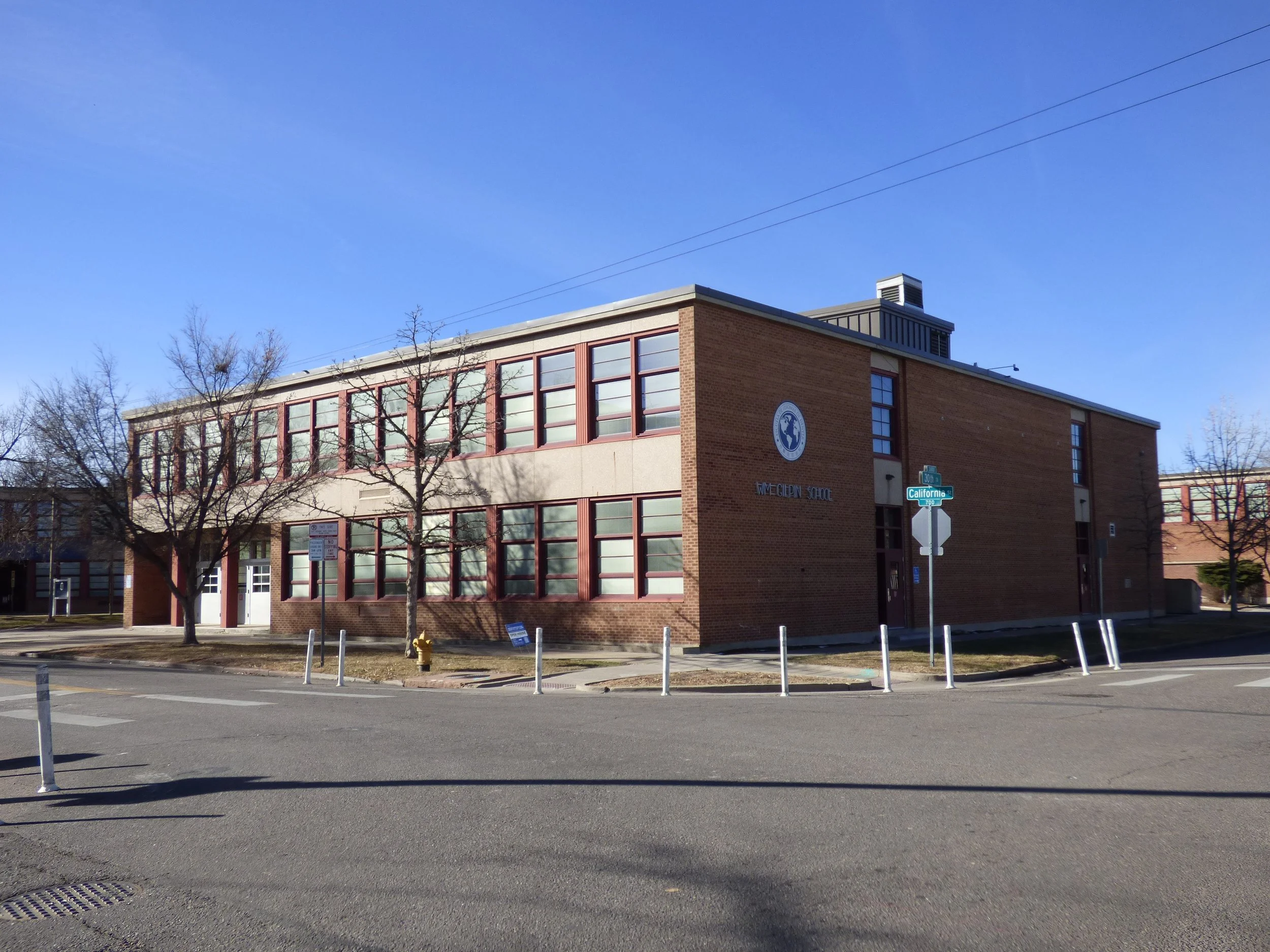 A two-story brick building with large windows and a sign that reads 'WIC-CHILDREN'S' on the front, located at the corner of a street with street signs for California and 21st Streets, and some leafless trees in front.
