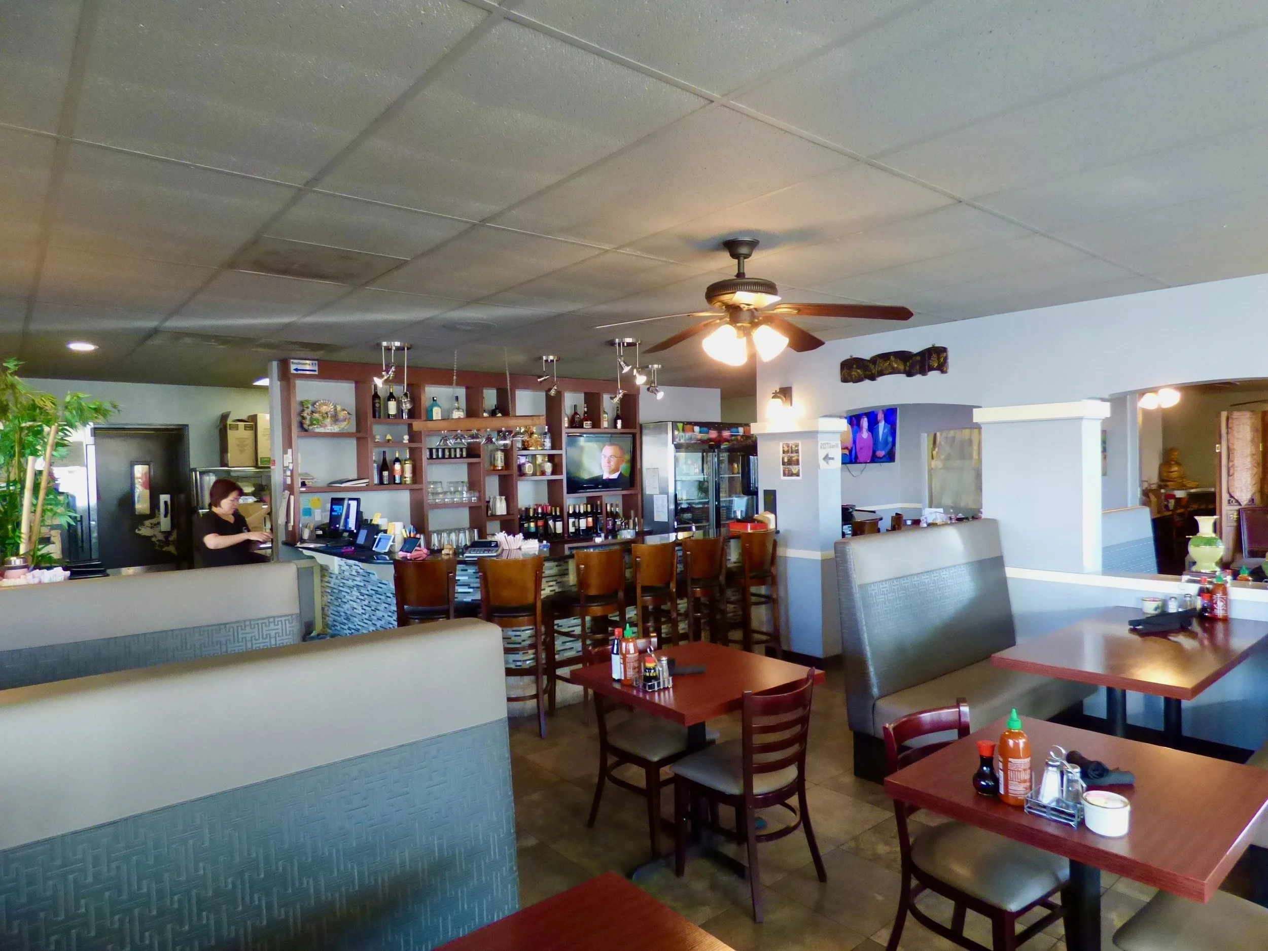 Interior of a restaurant with tables, chairs, a bar area, and a ceiling fan.