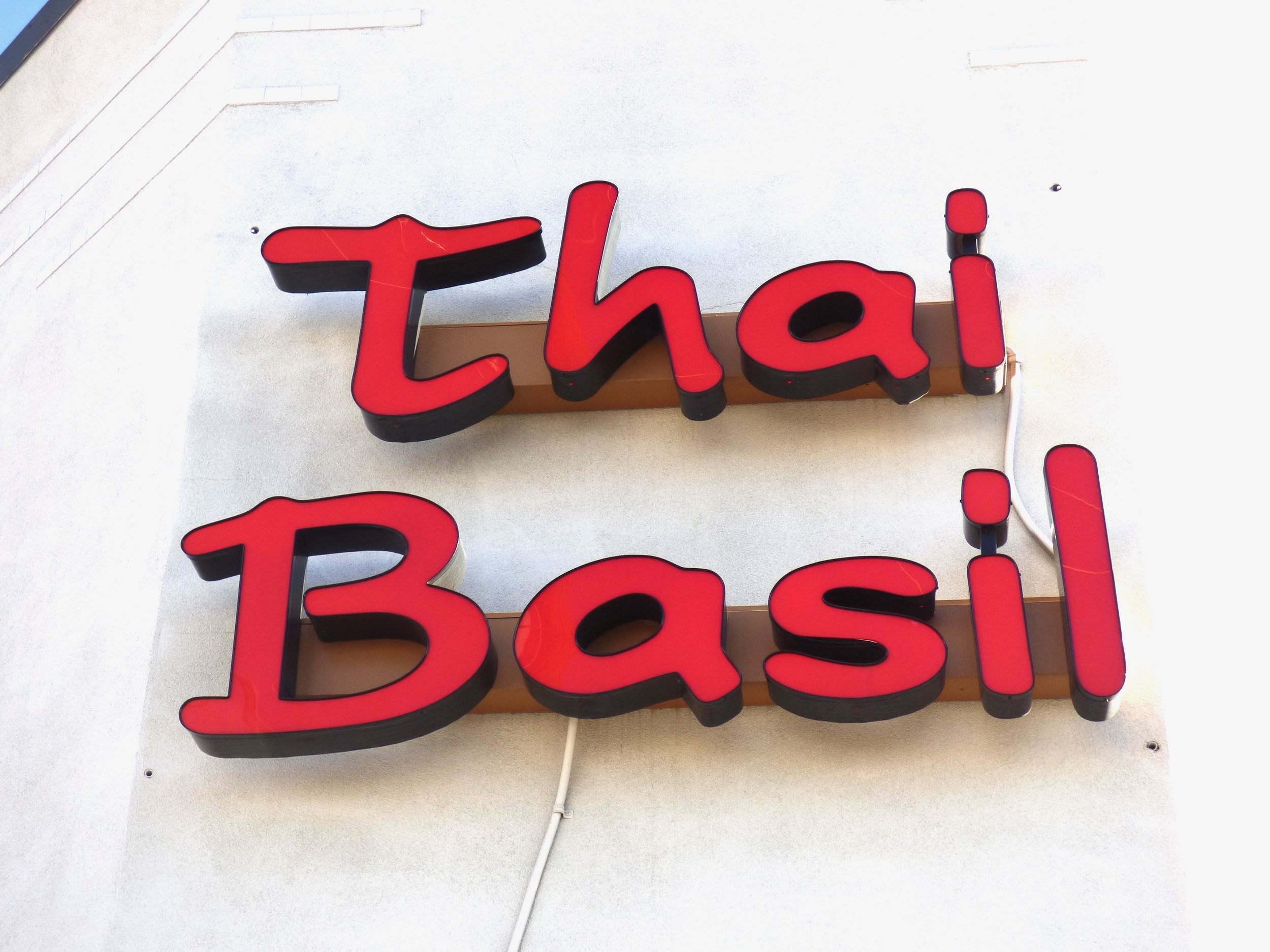 Red illuminated sign saying 'Thai Basil' attached to a beige wall.