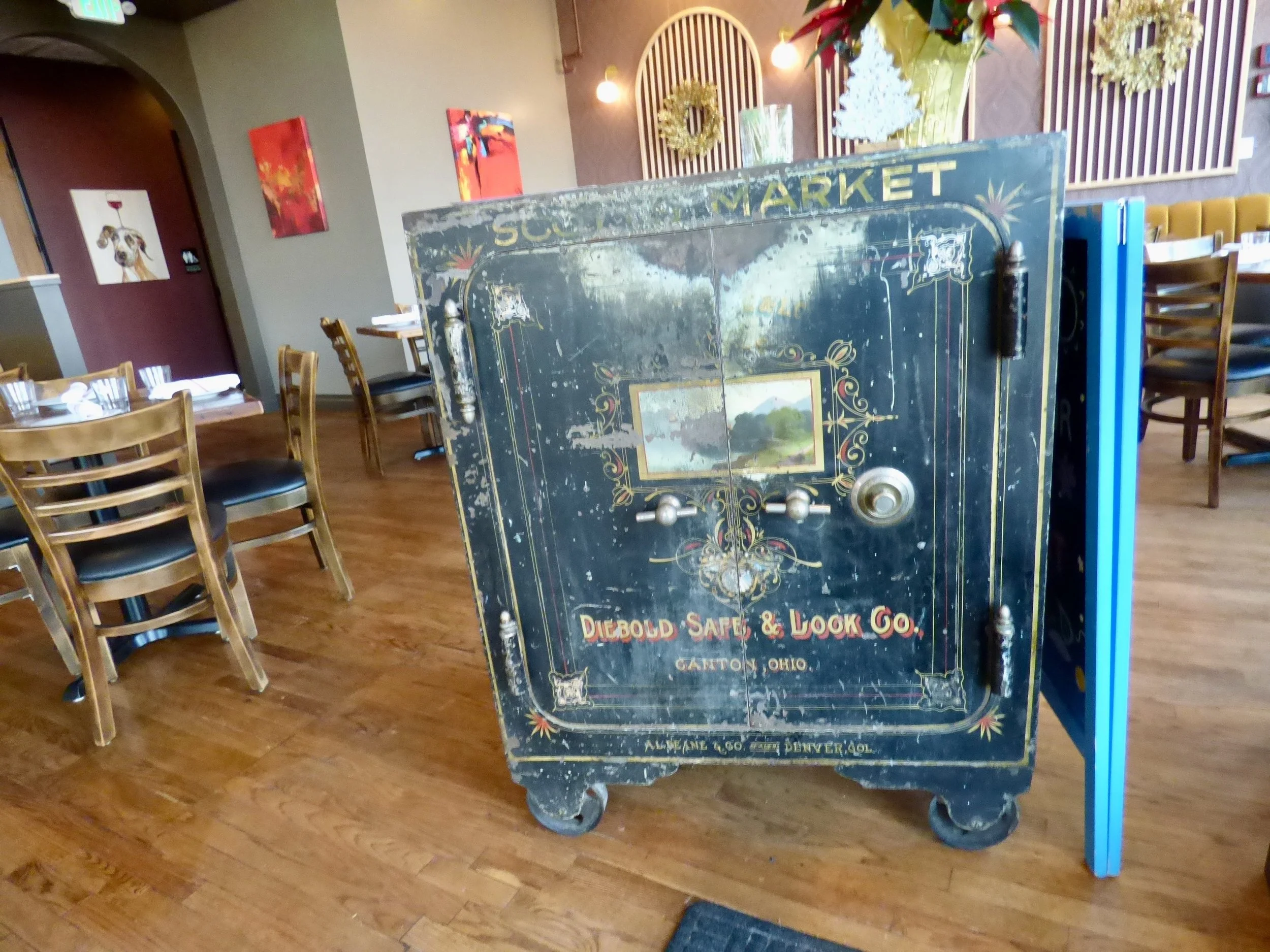 An antique black safe with decorative gold and red details, including a small landscape painting in the center, placed in a restaurant at Whit's End, Denver, CO 80205.