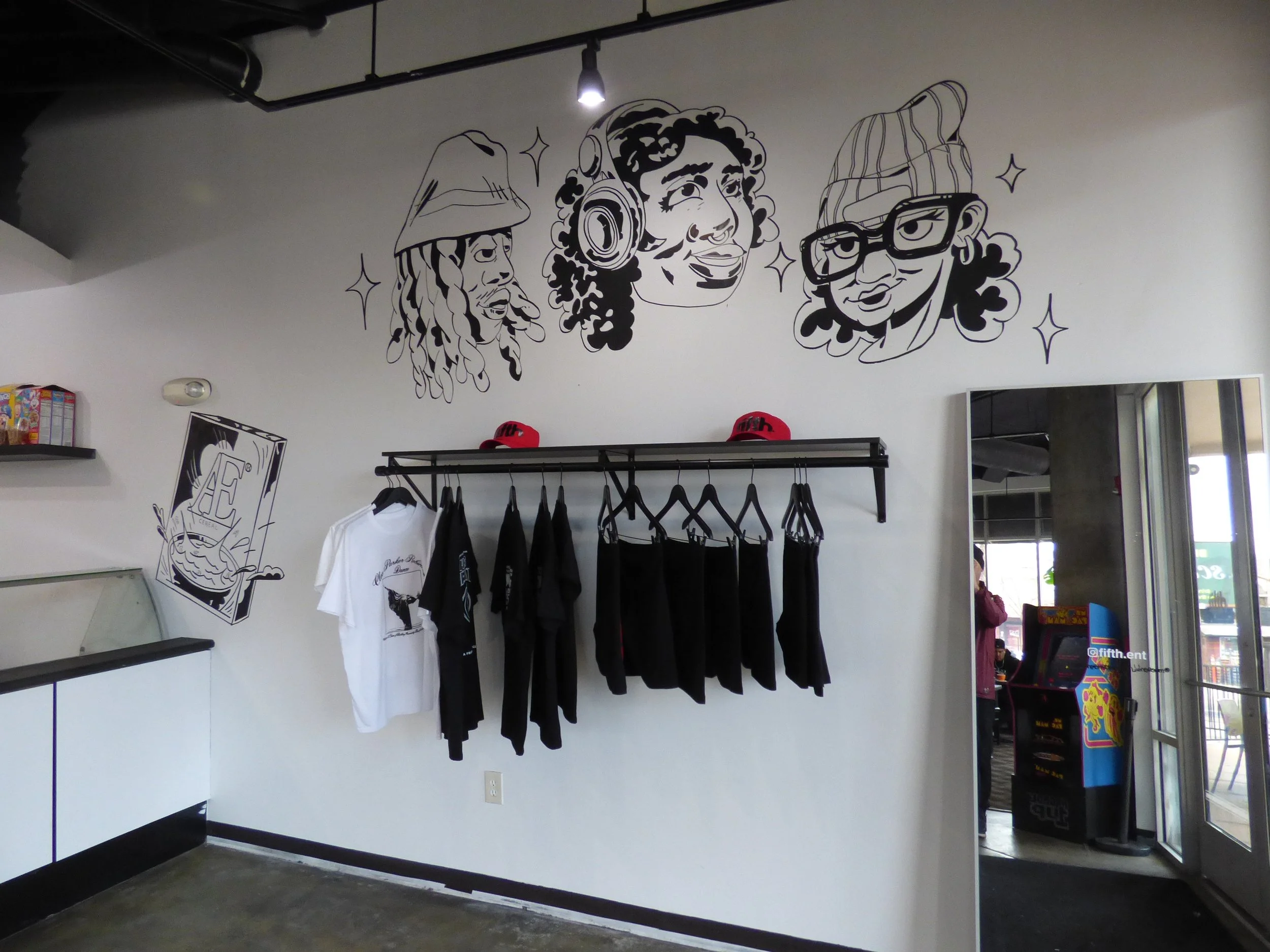 Black and white wall art of three illustrated faces above a clothing display in a retail store at Fifth Coffee House, Denver, CO 80205.