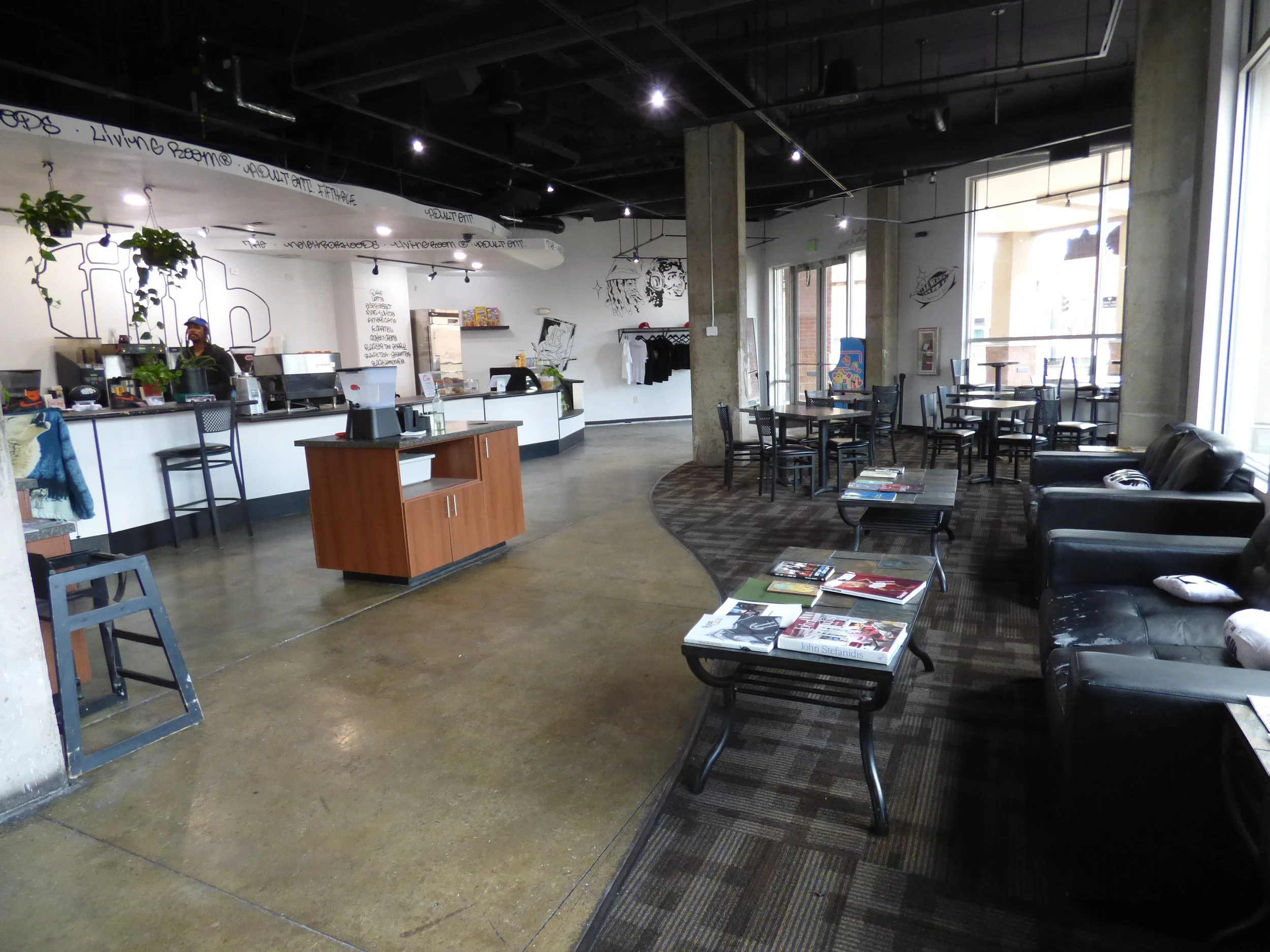 Interior of a cafe with a coffee counter, seating area with tables and chairs, and a sofa with magazines on the tables Fifth Coffee House, Denver, CO 80205.