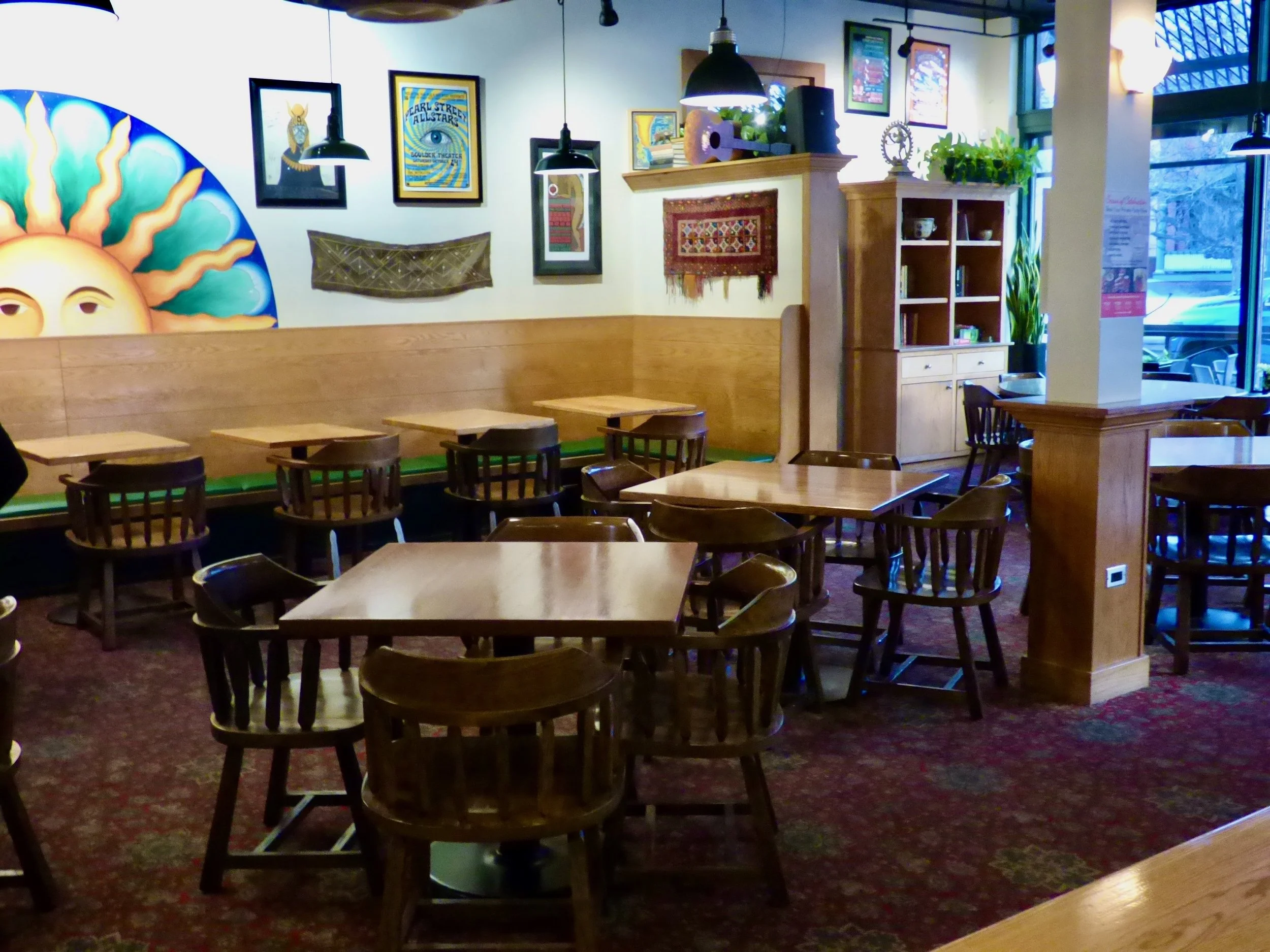 Empty cozy restaurant or cafe with wooden tables and chairs, colorful artwork and decorations on the walls, and large windows letting in natural light at Vine Street Pub, Denver, CO.