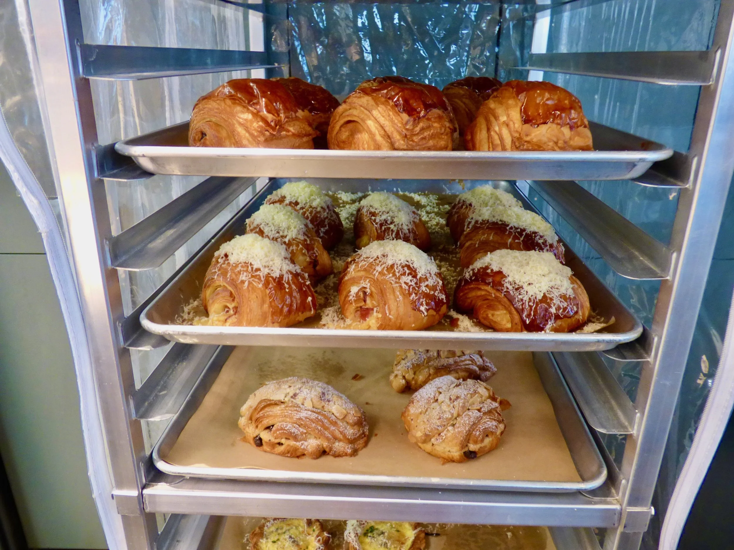Shelves with croissants and pastries in a bakery display case at Elemental Bakery & Coffeehouse, Denver, CO 80205.