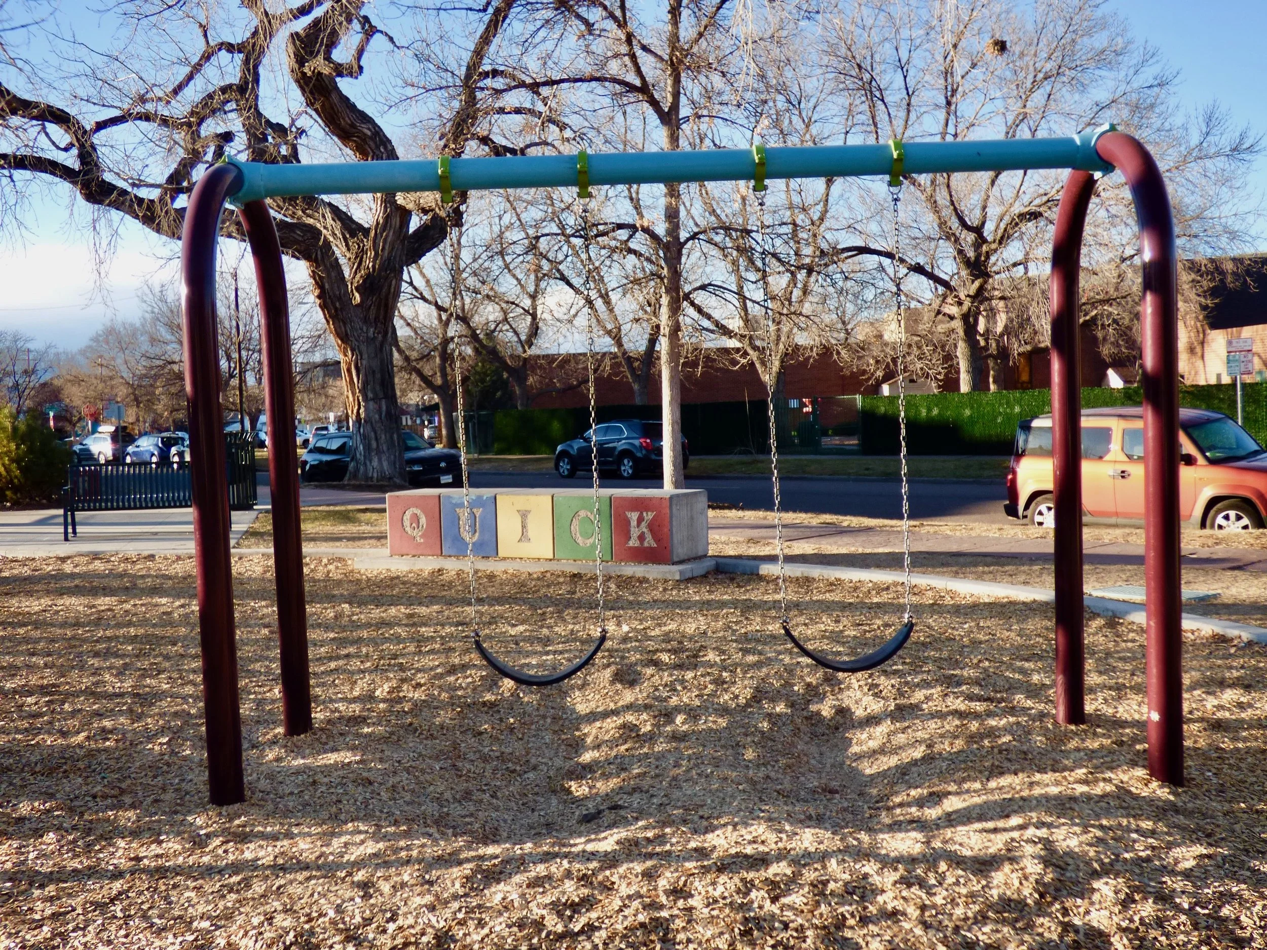 Empty playground in daylight with two swings and colorful blocks in the background."