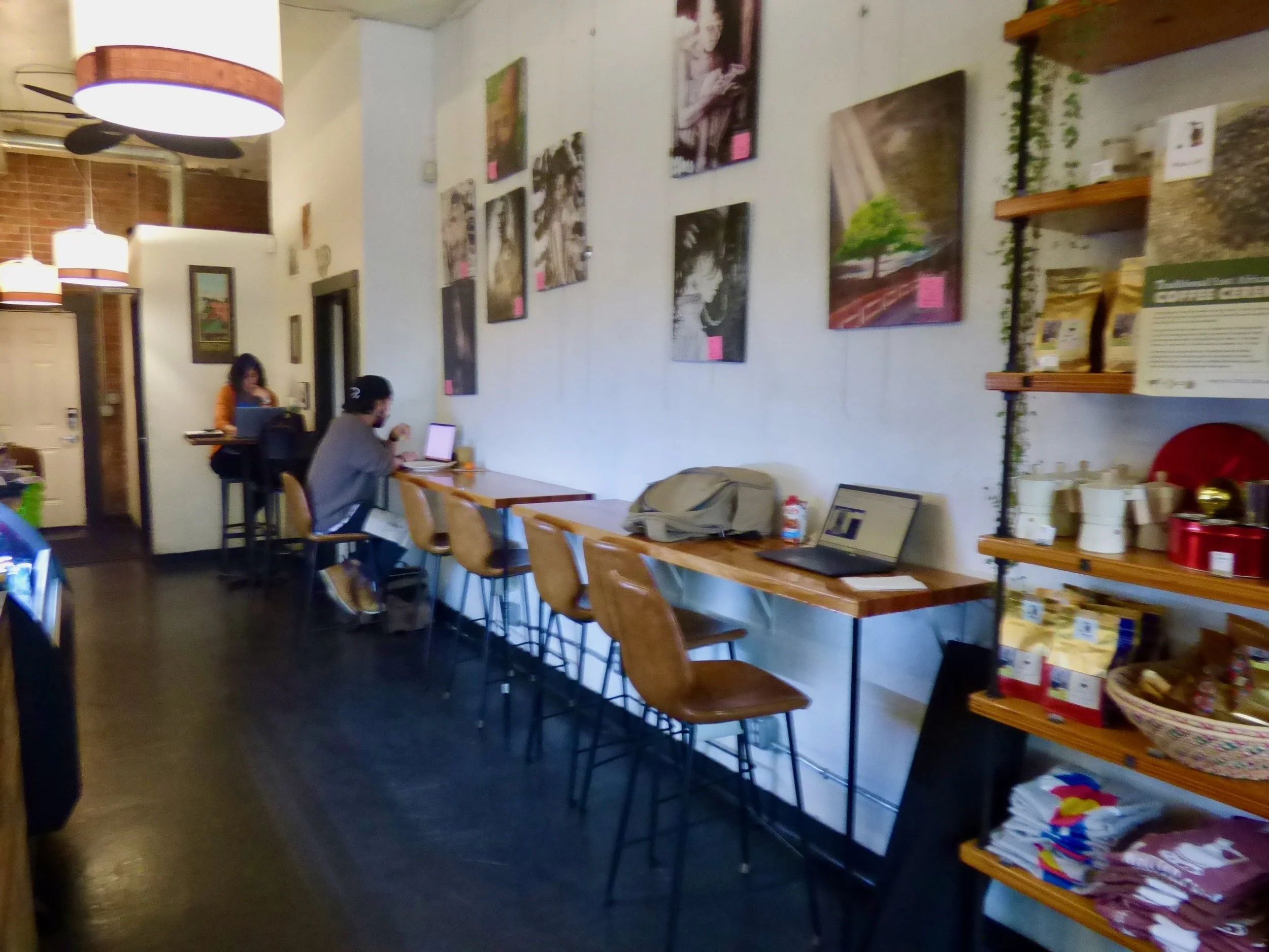 Interior of a cozy cafe with white walls decorated with framed artwork, wooden ceiling fans, and hanging lamps at Whittier Cafe, Denver, CO 80205.