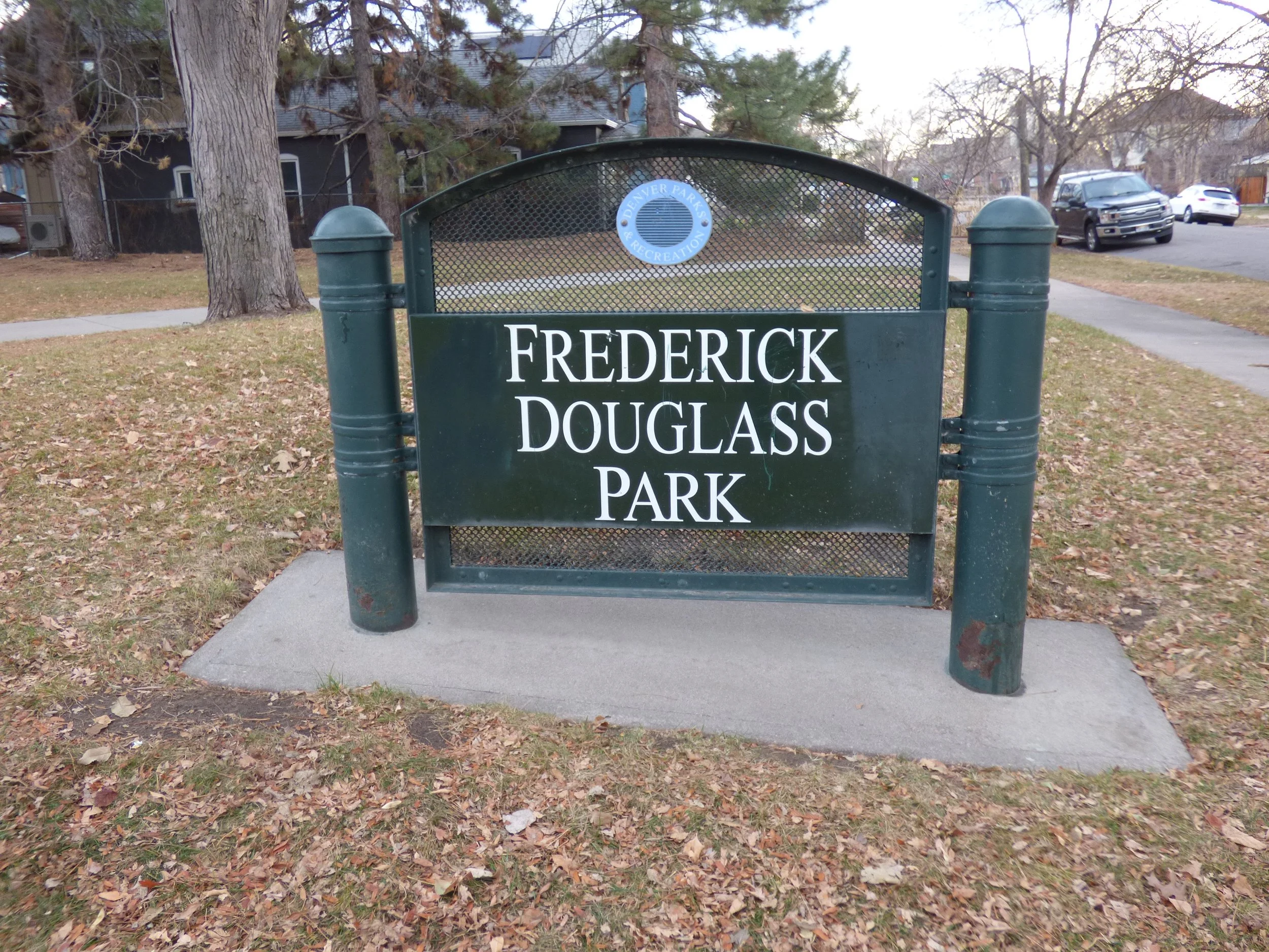 Sign for Frederick Douglass Park with trees and parked cars in the background at Frederick Douglas Park, Denver, CO 80205.