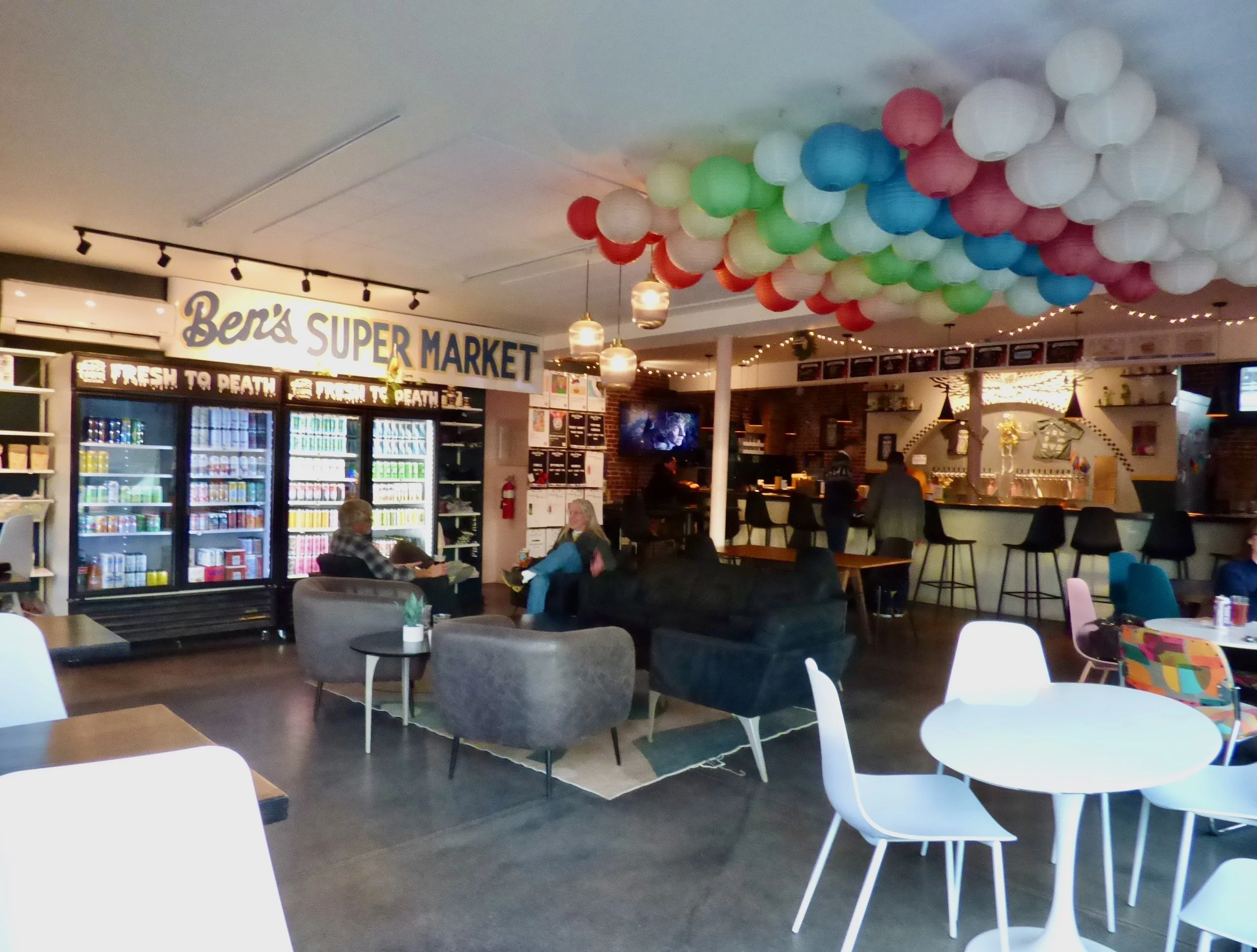Interior of a casual cafe with a bar, seating area, and colorful paper lanterns hanging from the ceiling at Ephemeral Rotating Taproom, Denver, CO 80205.