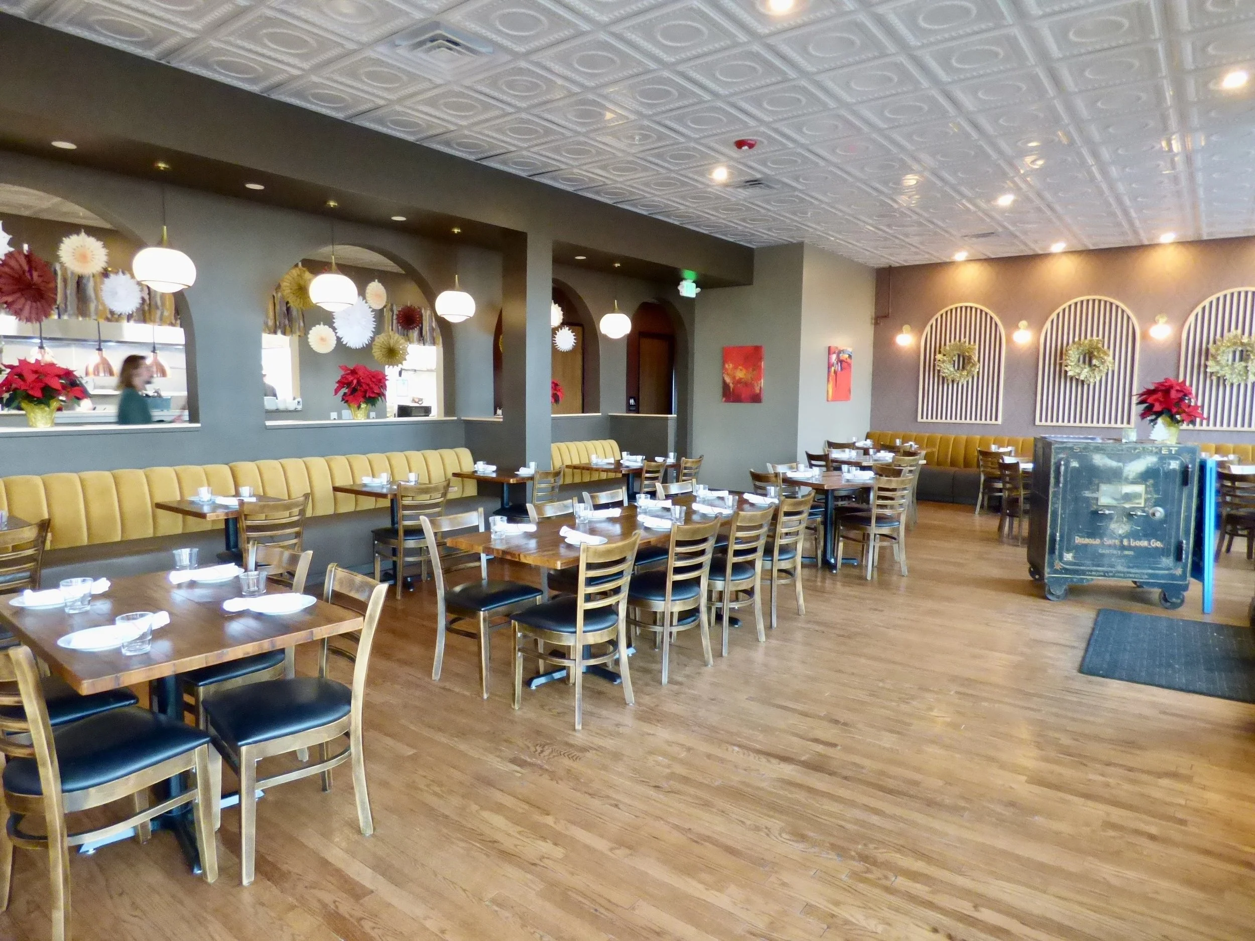Interior of a restaurant decorated with Christmas wreaths and poinsettias, with tables set for dining and a safe in the corner at Whit's End, Denver, CO 80205.