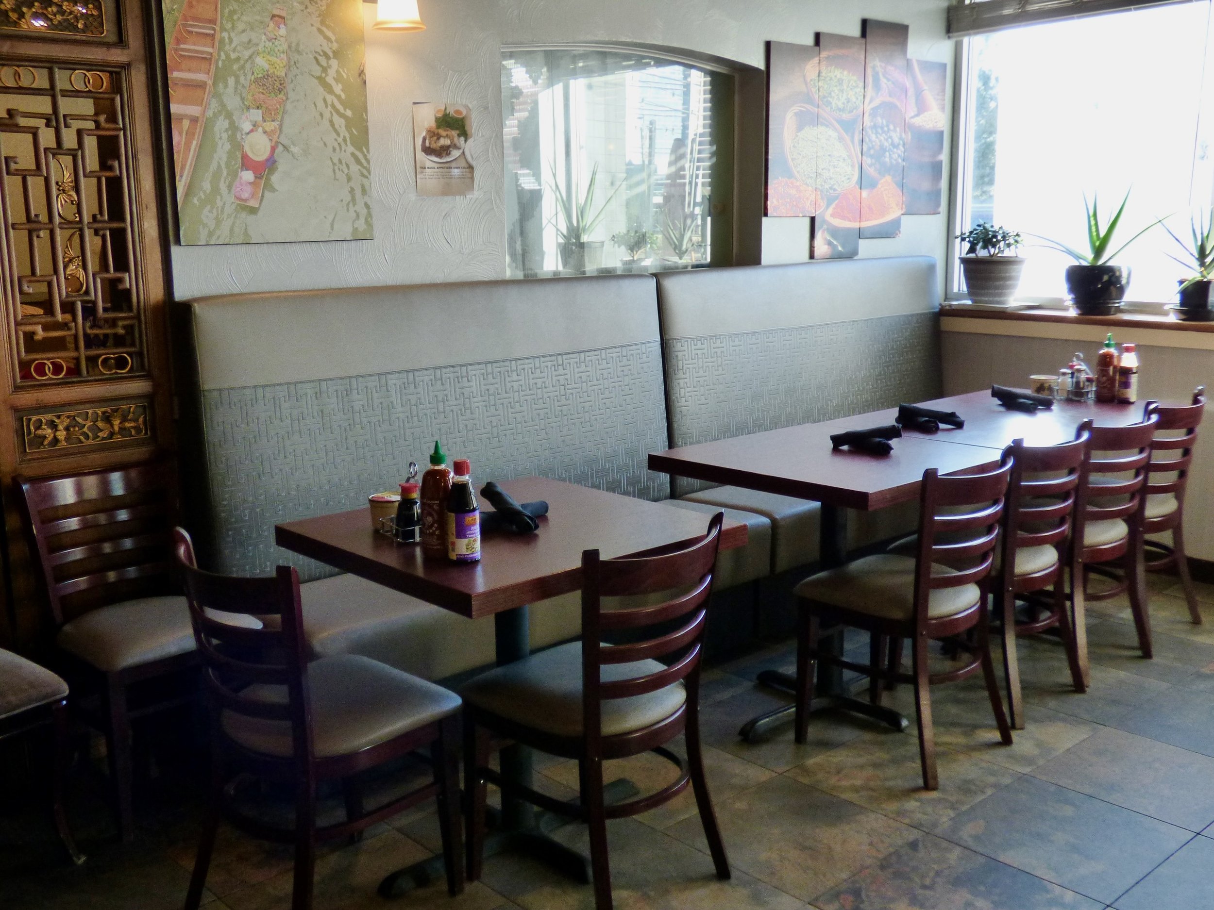 Empty restaurant booth with tables, chairs, condiments, and artwork on the walls.