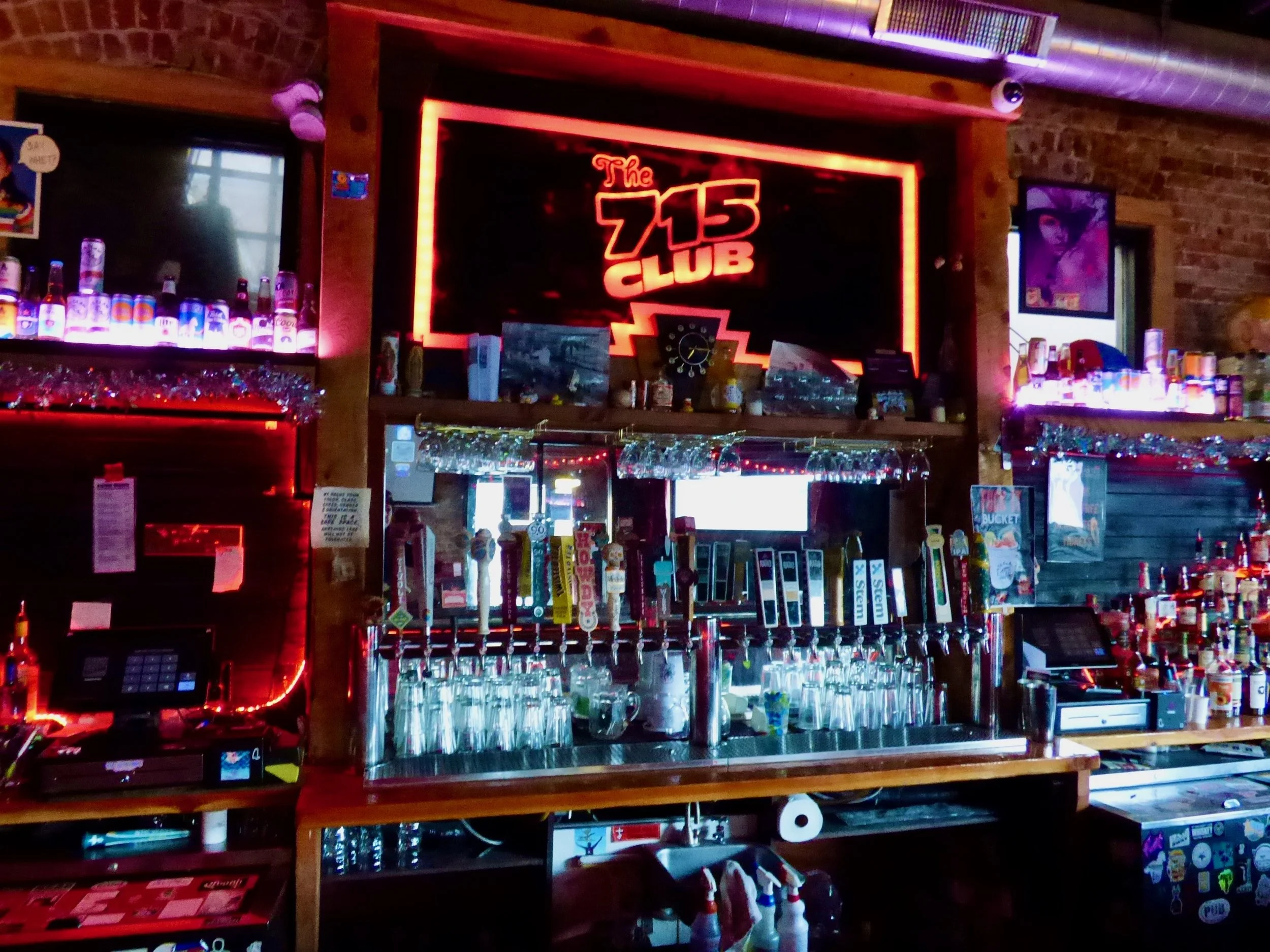 The bar area of The 715 Club with neon sign, beer taps, and various bottles and decorations at 715 Club, Denver, CO 80205.