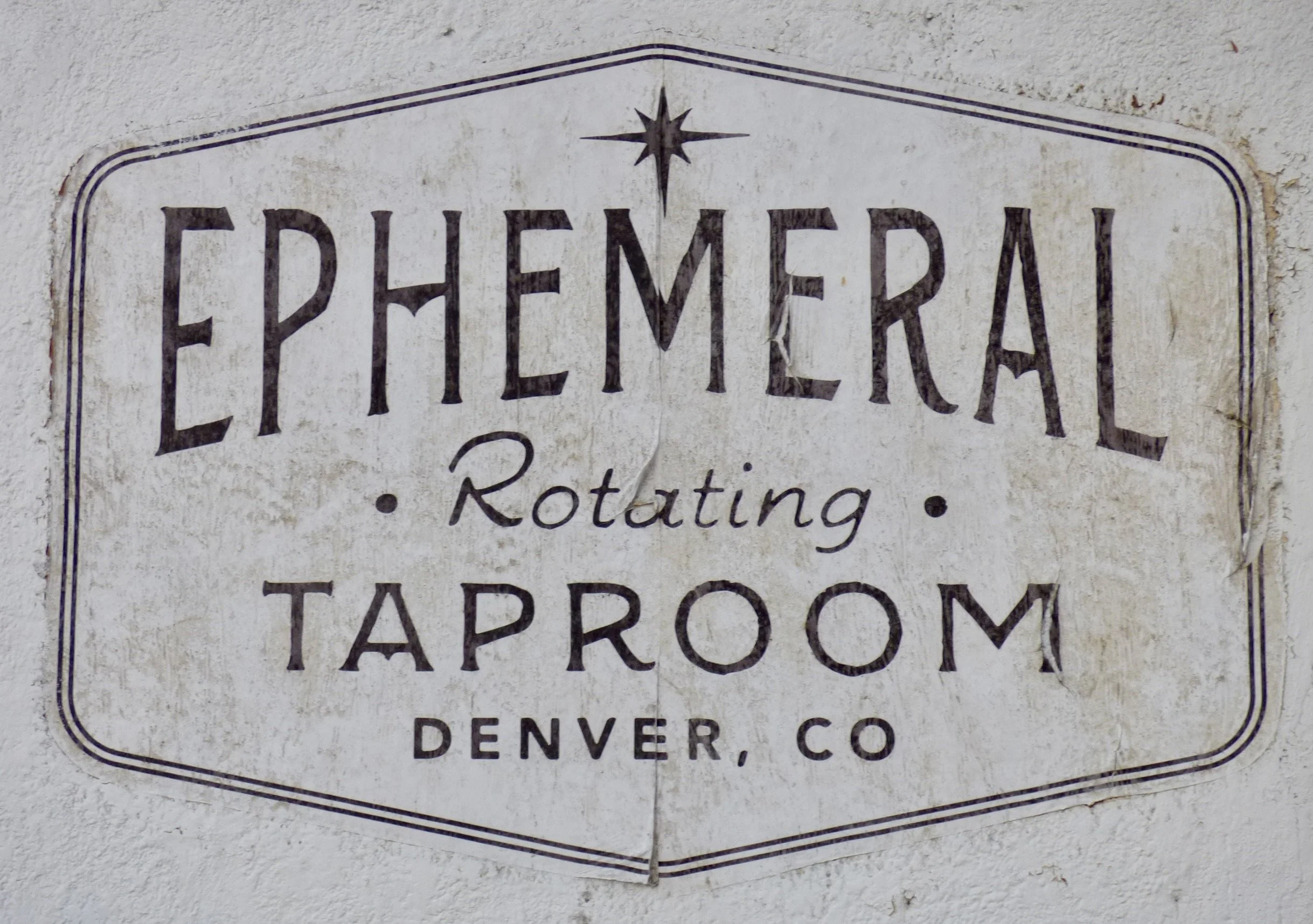 A vintage sign for a tavern in Denver, Colorado, featuring the words 'Euphemeral Rotating - Taproom' with a star at the top, on a textured white wall at Ephemeral Rotating Taproom, Denver, CO 80205.