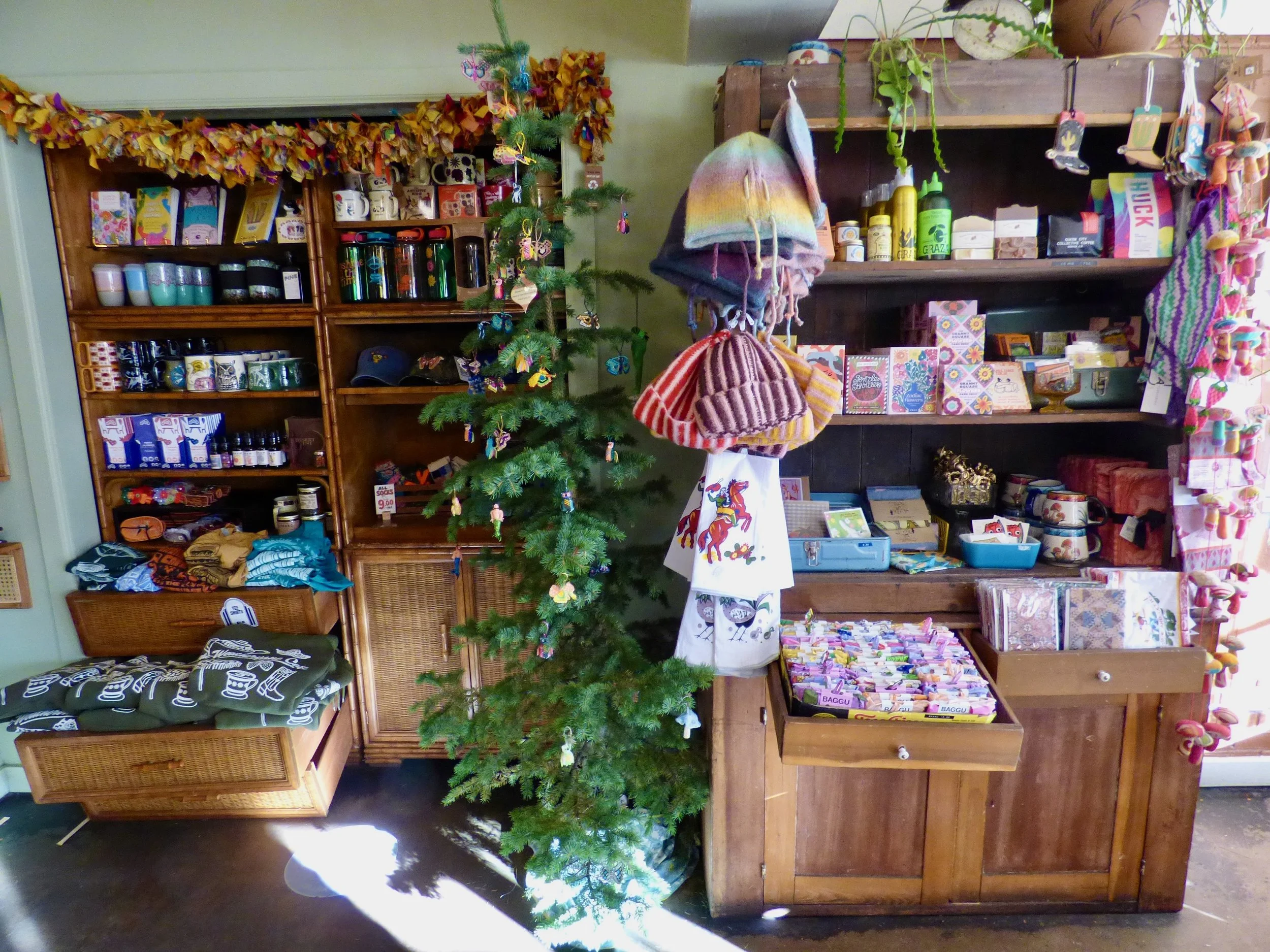 Interior of a gift shop with shelves displaying various merchandise, a decorated Christmas tree, and colorful hats hanging from a wooden structure at Weathervane Cafe, Denver, CO.