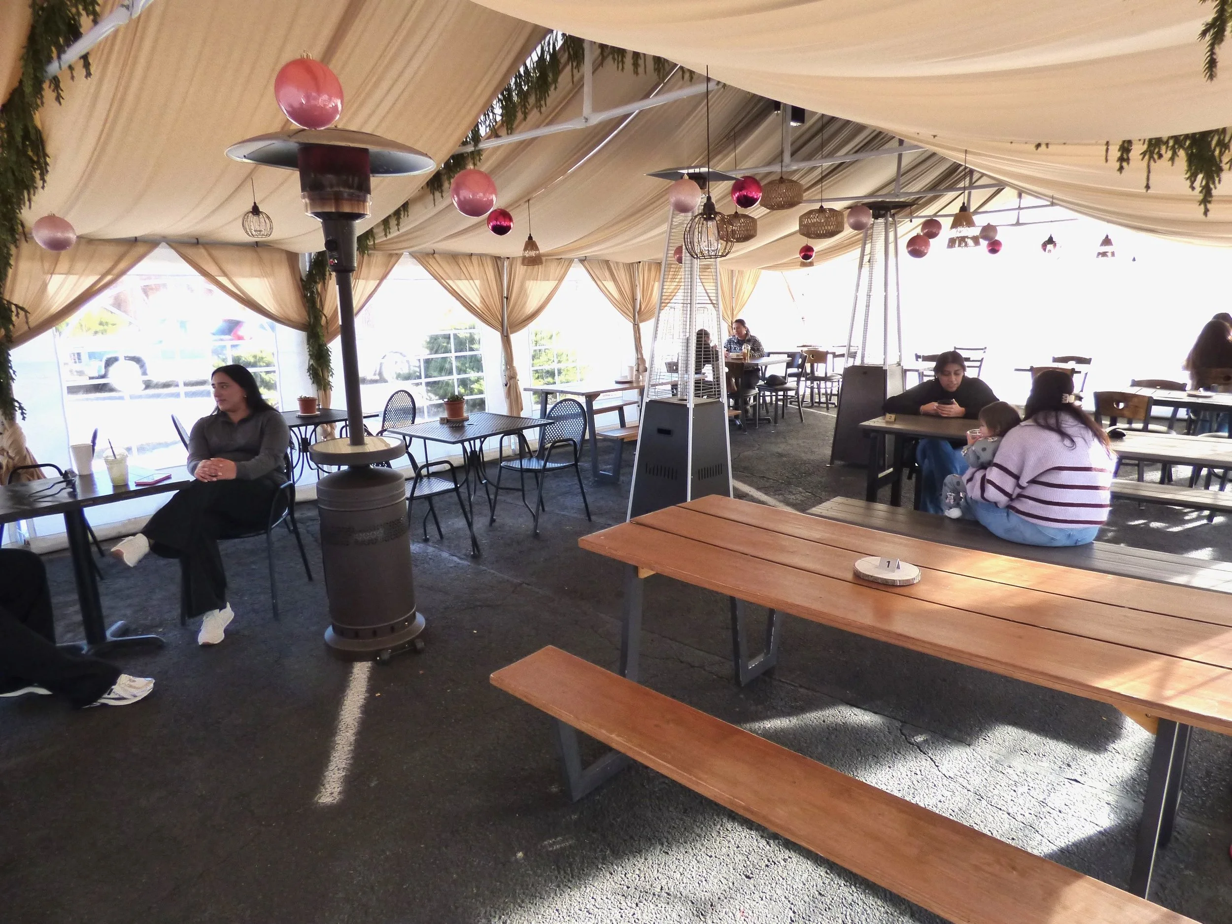 People seated at tables in a large, decorated outdoor or semi-outdoor event space with draped fabric ceiling and hanging ornaments at Oasis Cafe & Grill, Denver, CO 80205.