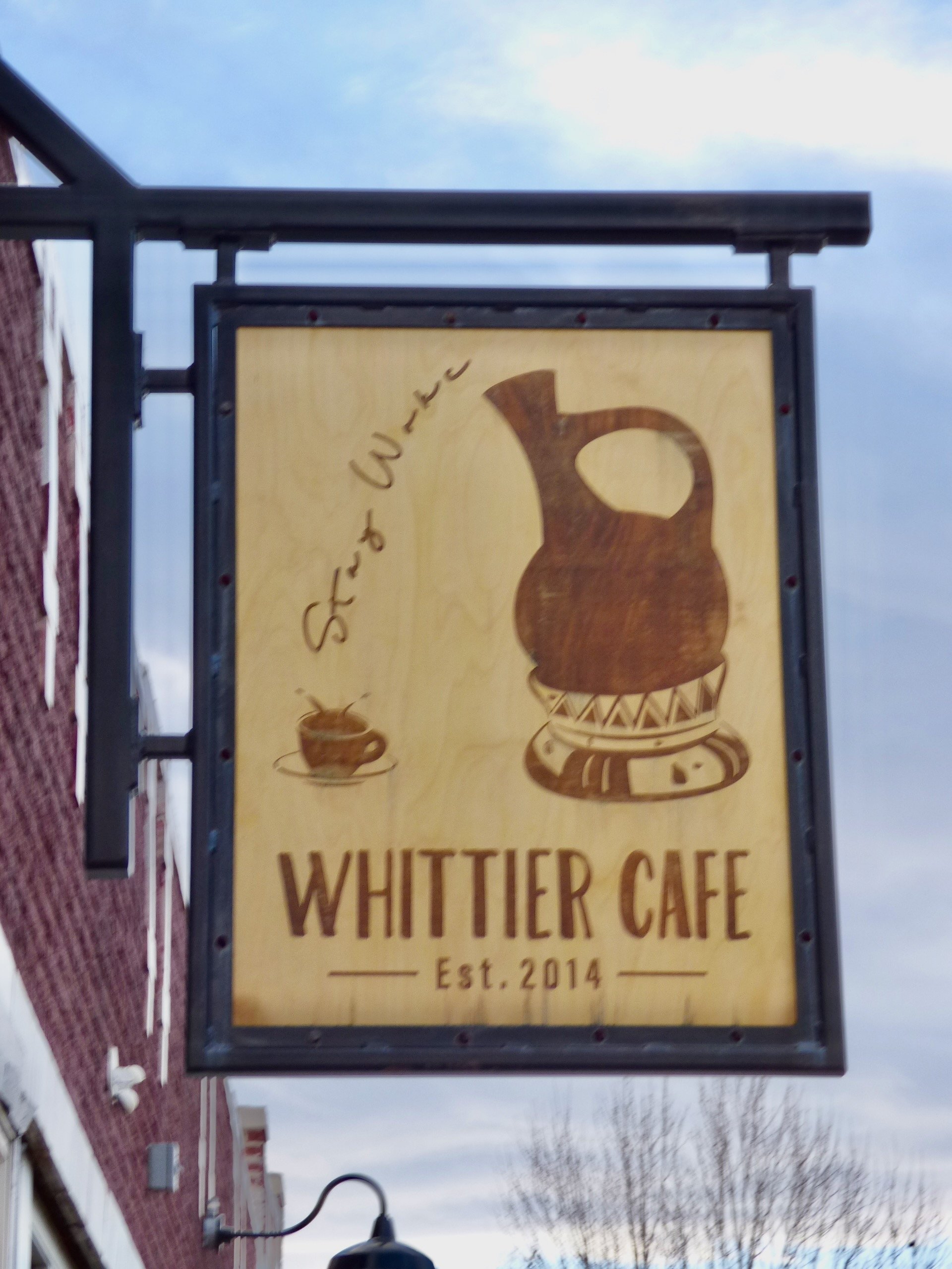 Signboard for Whittier Cafe with a wooden background, featuring a graphic of a coffee pot, a coffee cup, and the slogan "Stay & Witte," established in 2014 at Whittier Cafe, Denver, CO 80205.