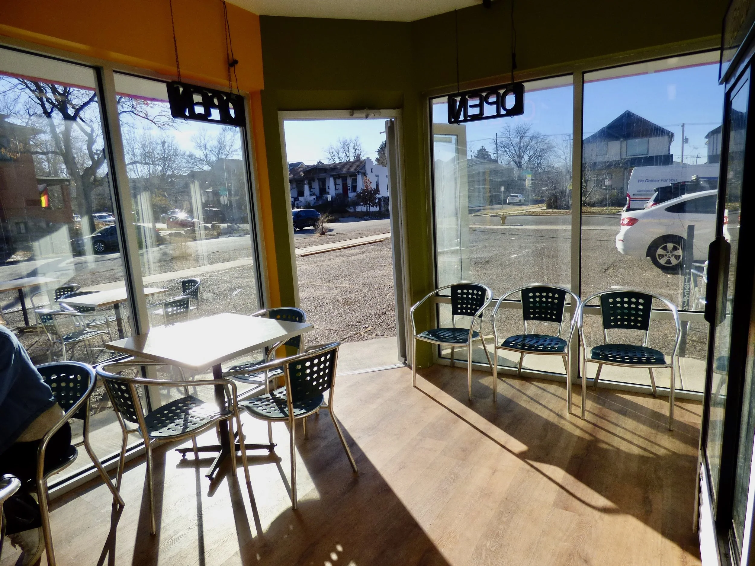 Empty cafe or restaurant with large glass windows, some chairs and tables, 'OPEN' and 'DEAR' signs hanging.