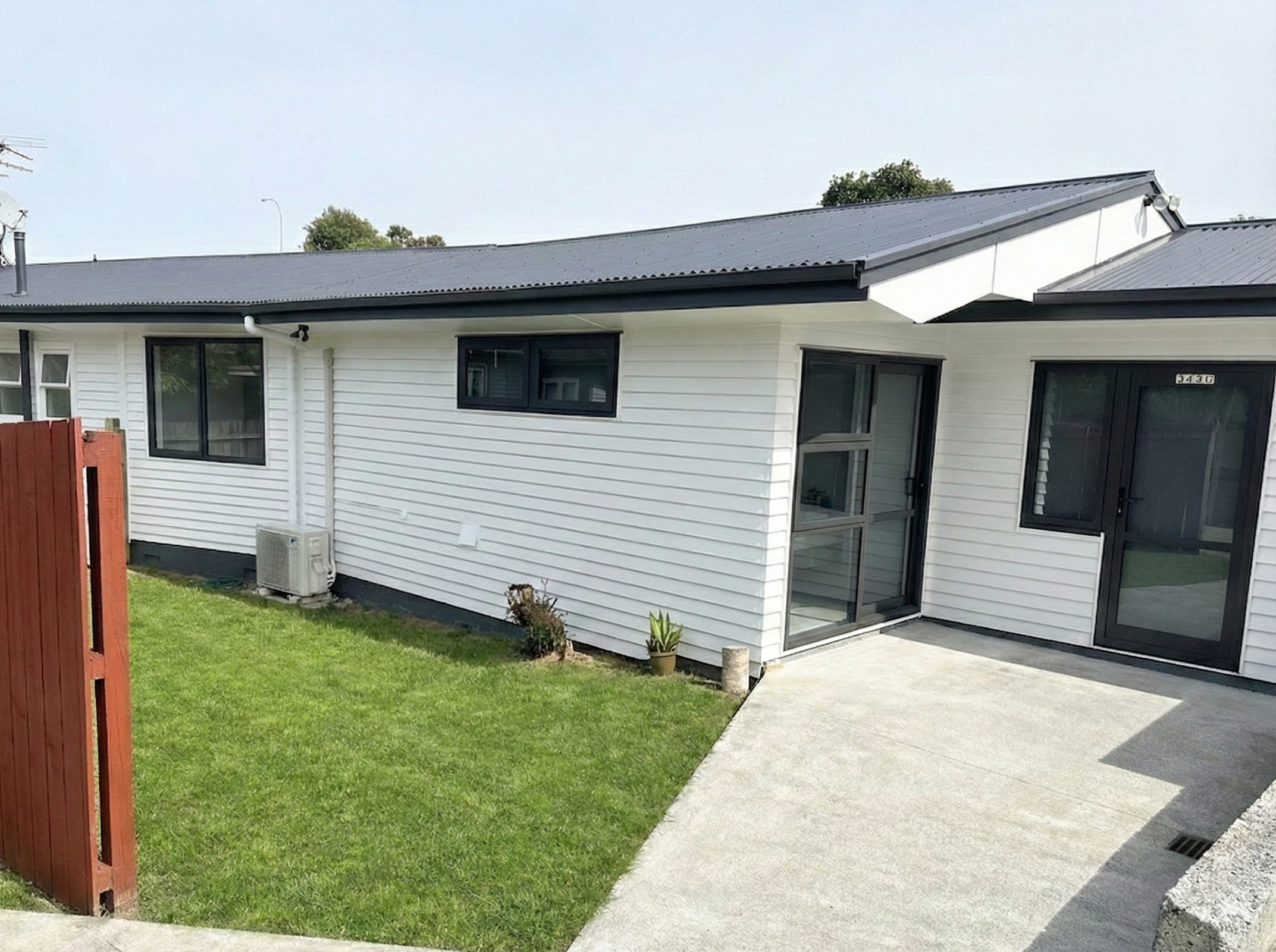 Exterior view of a modern house with white siding, black window frames, sliding glass door, small lawn, concrete patio, and red wooden fence.