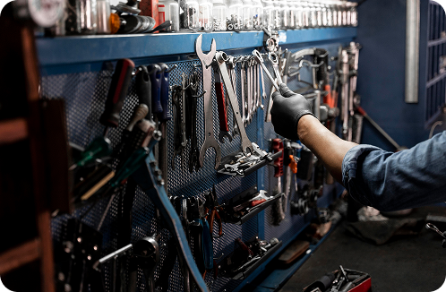 A person's hand wearing a black glove reaching for tools hanging on a blue pegboard in a workshop.
