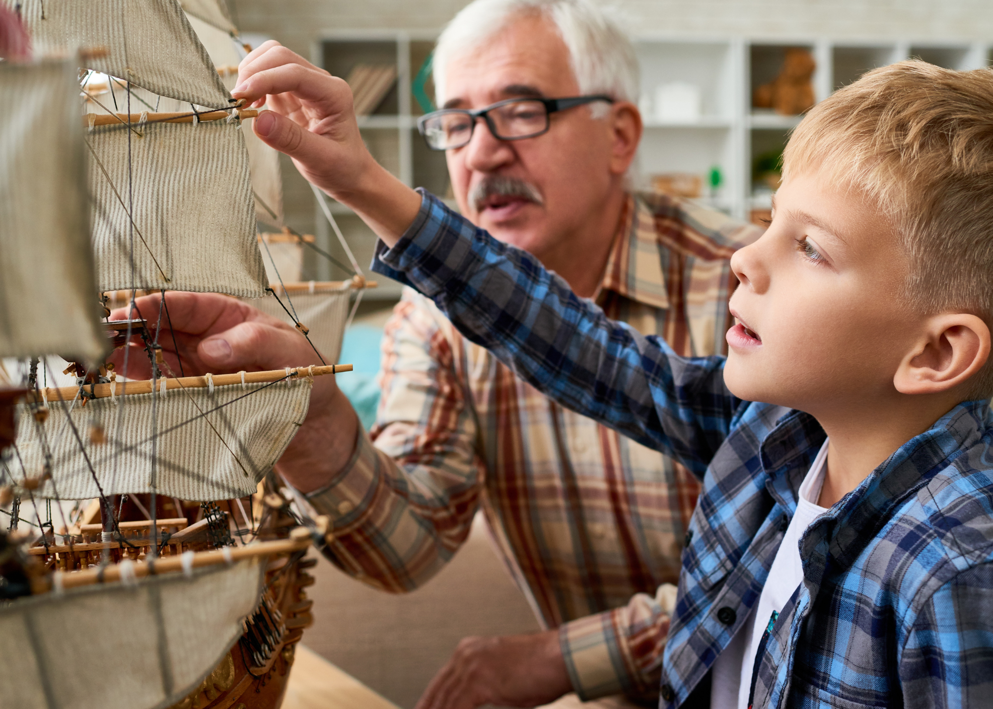 An elderly man with glasses and a young boy in a plaid shirt examining a detailed model of a sailing ship together.
