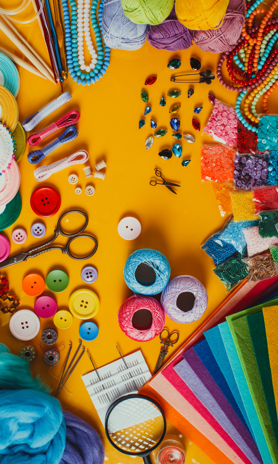 Crafting supplies including yarn, beads, buttons, scissors, needles, felt sheets, and decorative items on a yellow background.