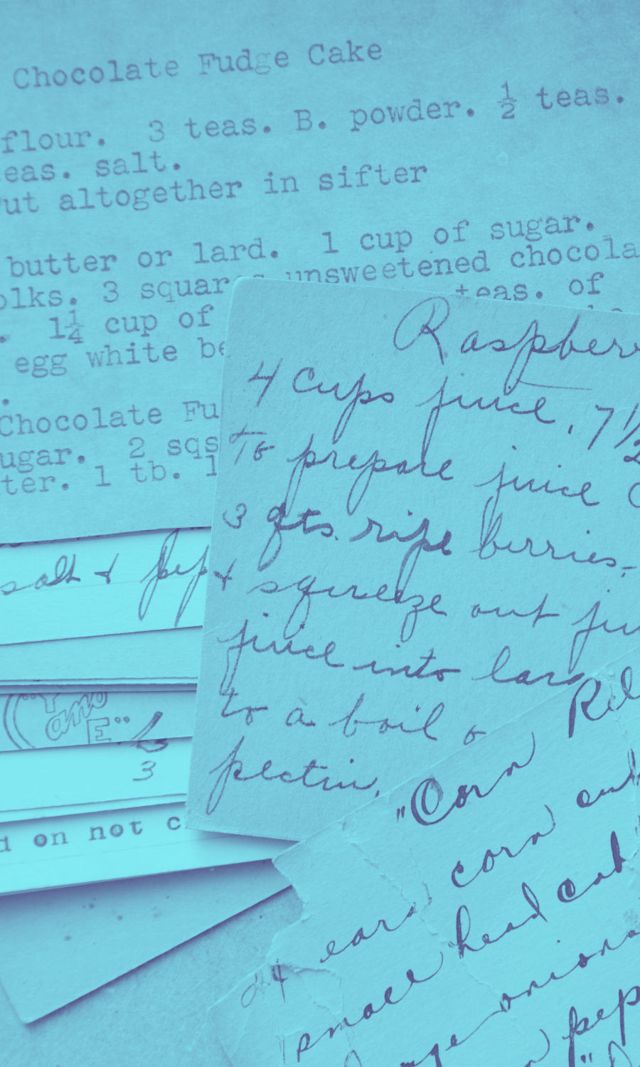 A collection of handwritten and printed recipes for chocolate fudge cake and raspberry sauce on blue paper.