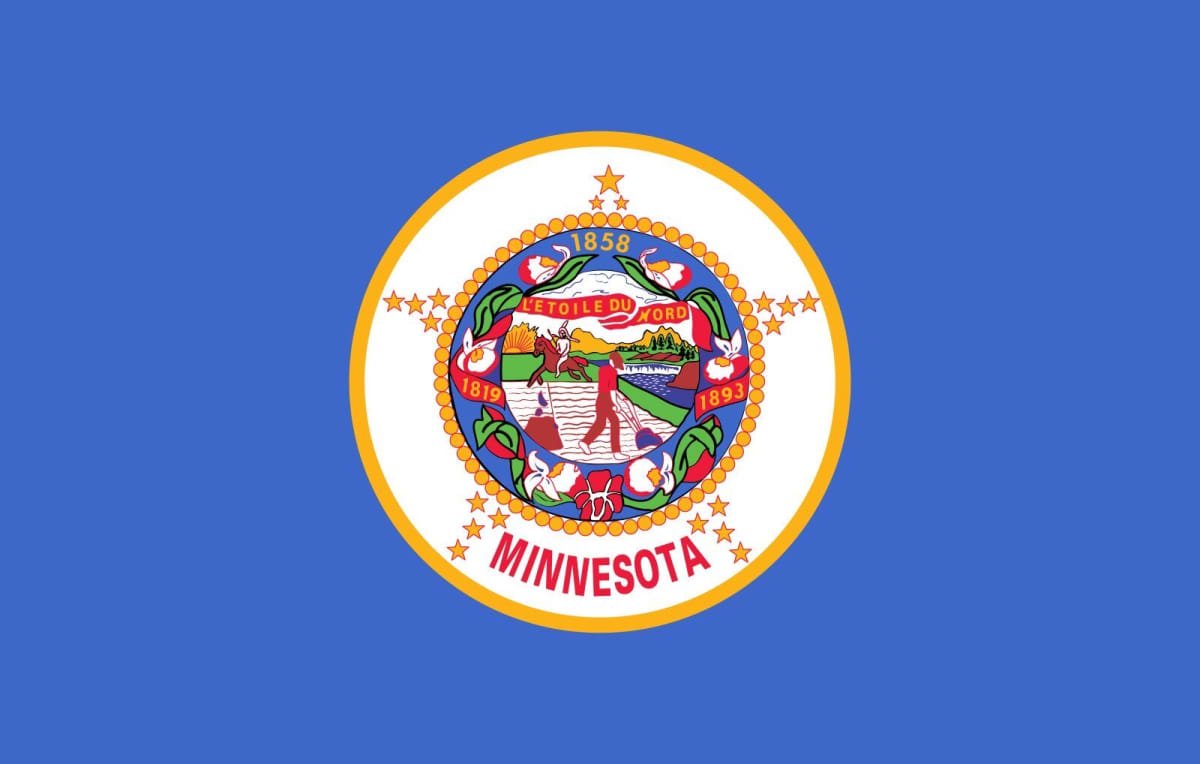 Flag of Minnesota featuring a blue background with a white circle in the center, displaying the Minnesota state seal surrounded by a gold border. The seal includes a farmer plowing a field, a river with a steamboat, and a Native American riding a horse, with the years 1858, 1819, and 1893. "MINNESOTA" is written below the seal in red.