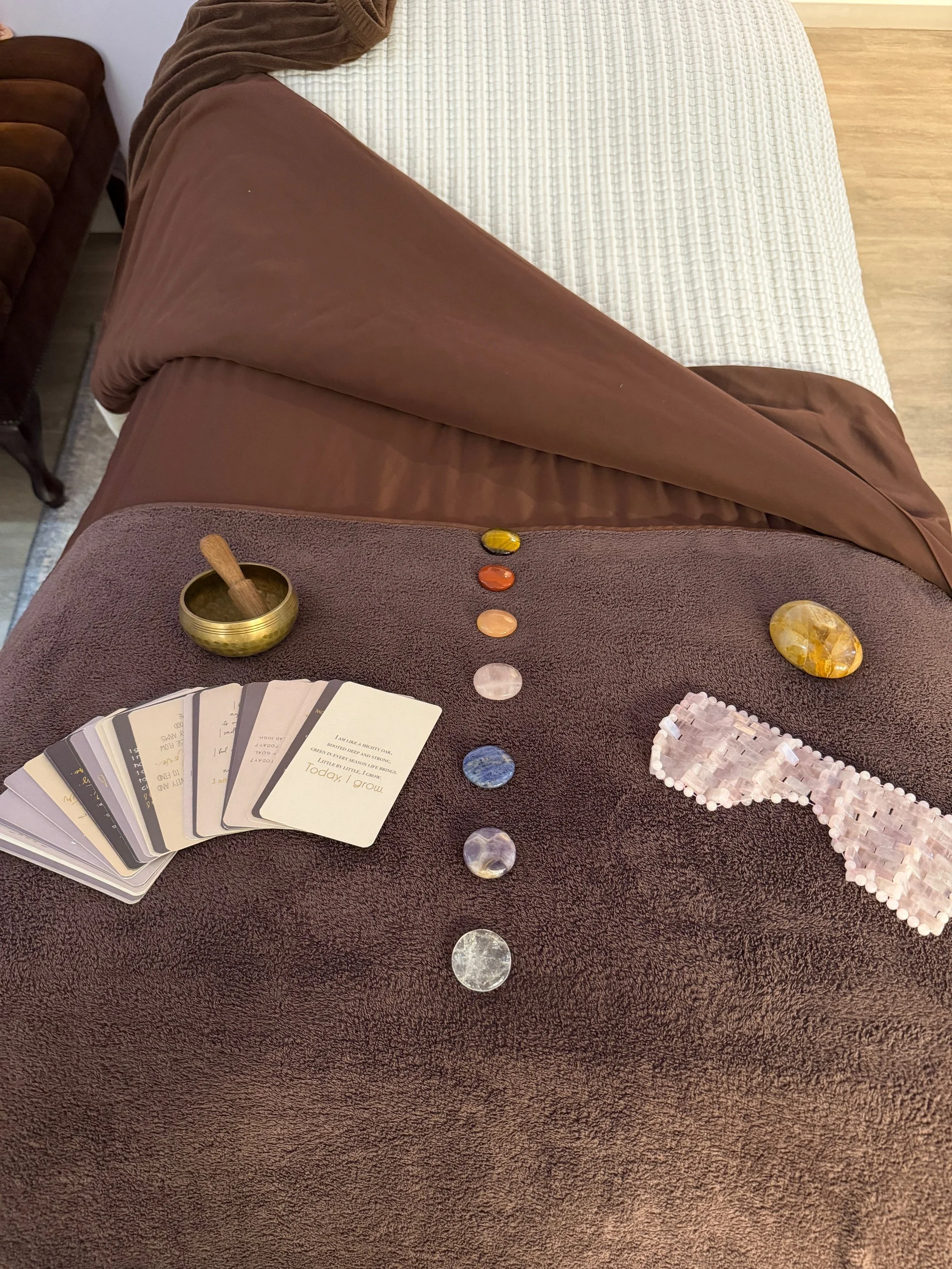 A table with Tarot cards, assorted crystals, a singing bowl with a mallet, and a pink beaded pyramid, arranged on a fuzzy brown cloth.