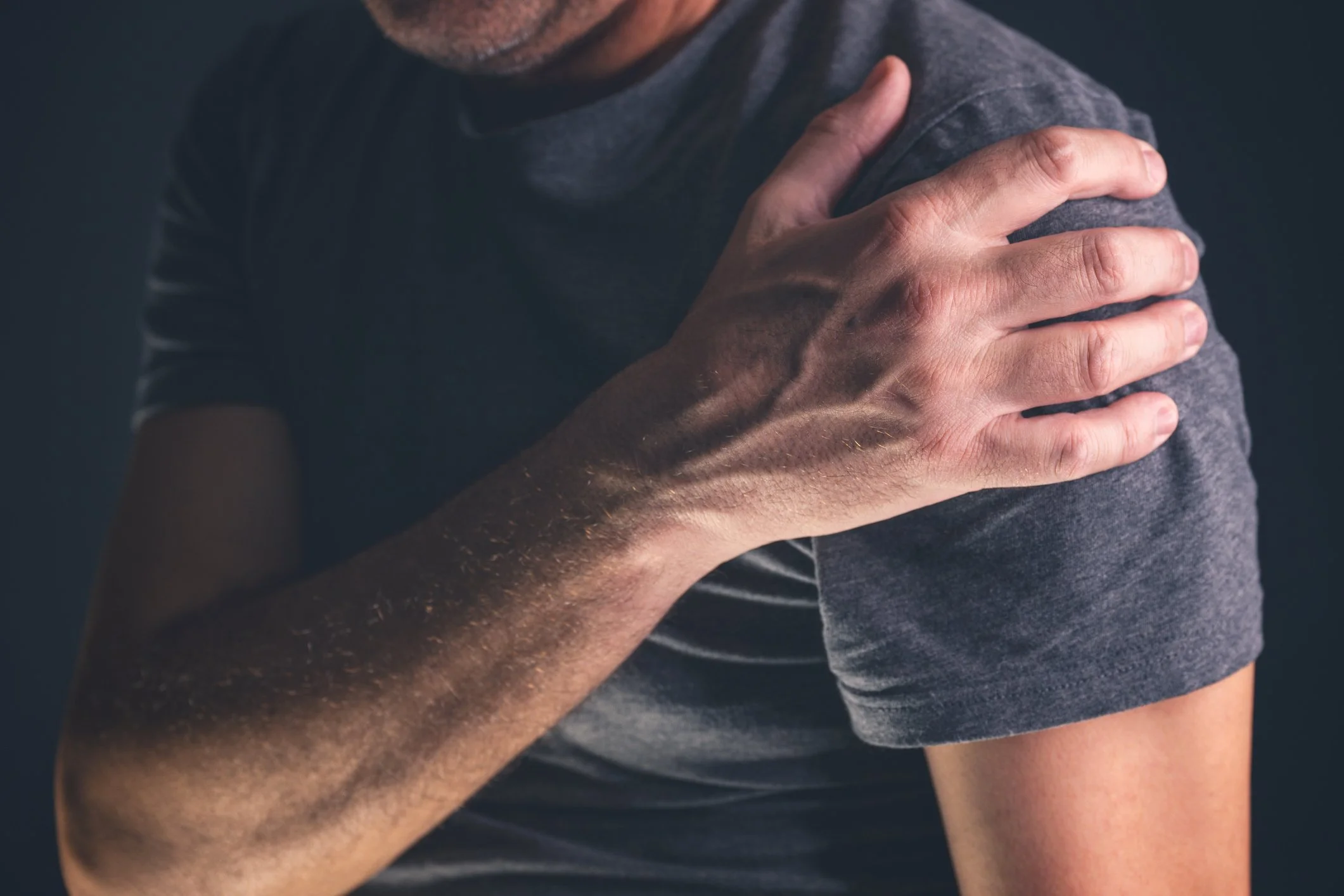 A man touching his shoulder, indicating shoulder pain or discomfort.