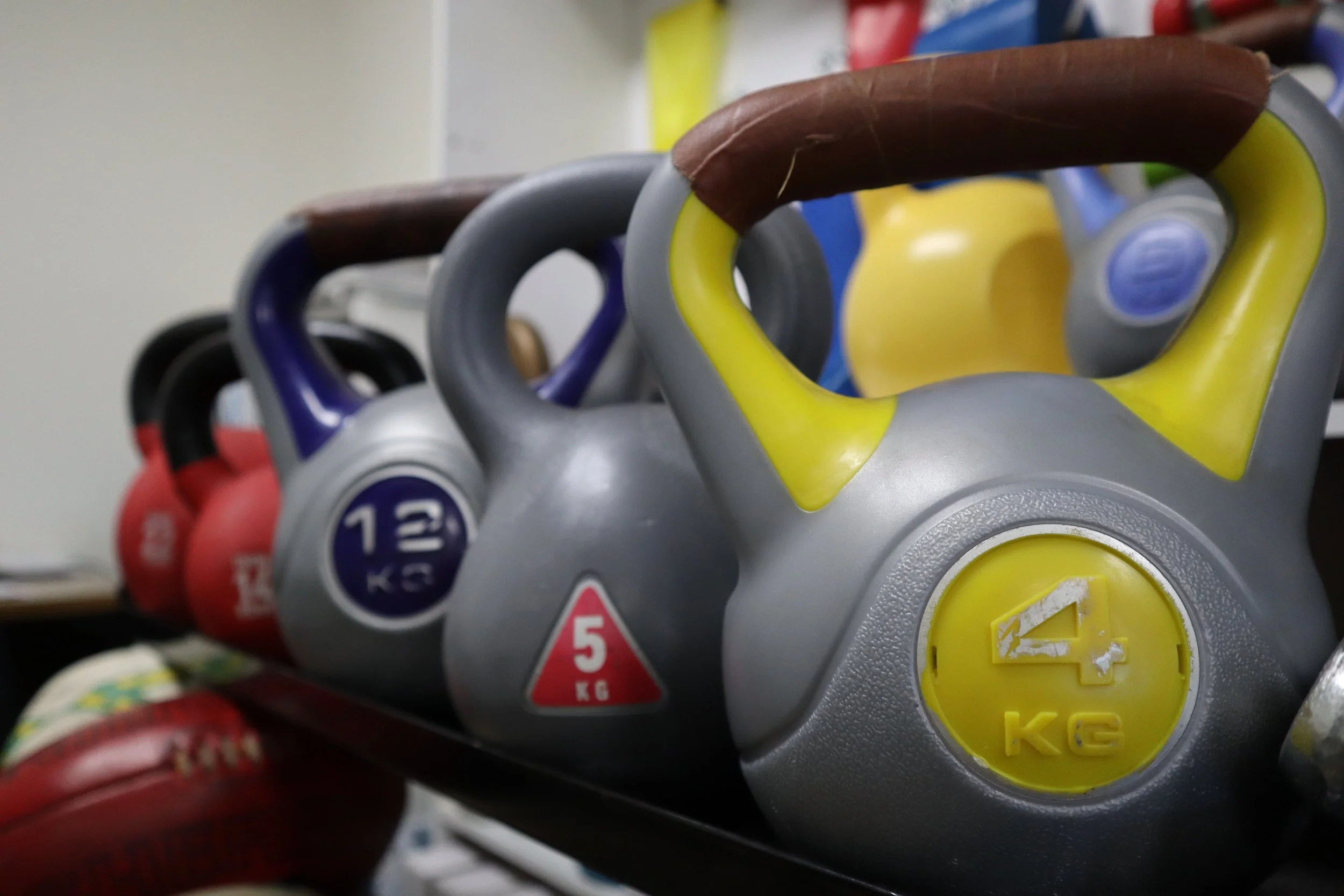 Row of colorful kettlebells on a black rack, with weights ranging from 4kg to 11kg, used for strength training.