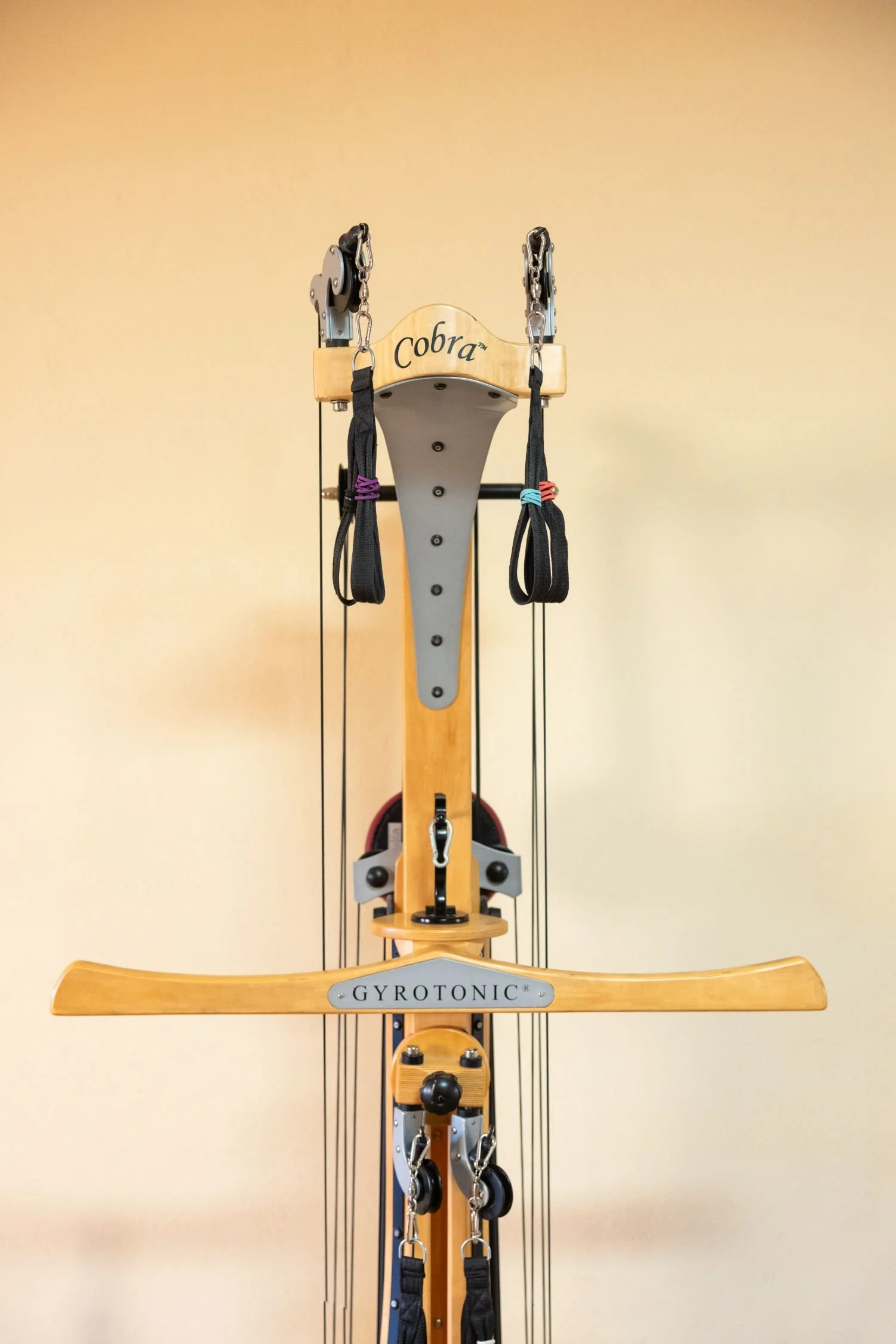 A wooden Pilates reformer machine with straps and pulleys, labeled with the brand names 'Cobra' and 'Gyrotonic'.