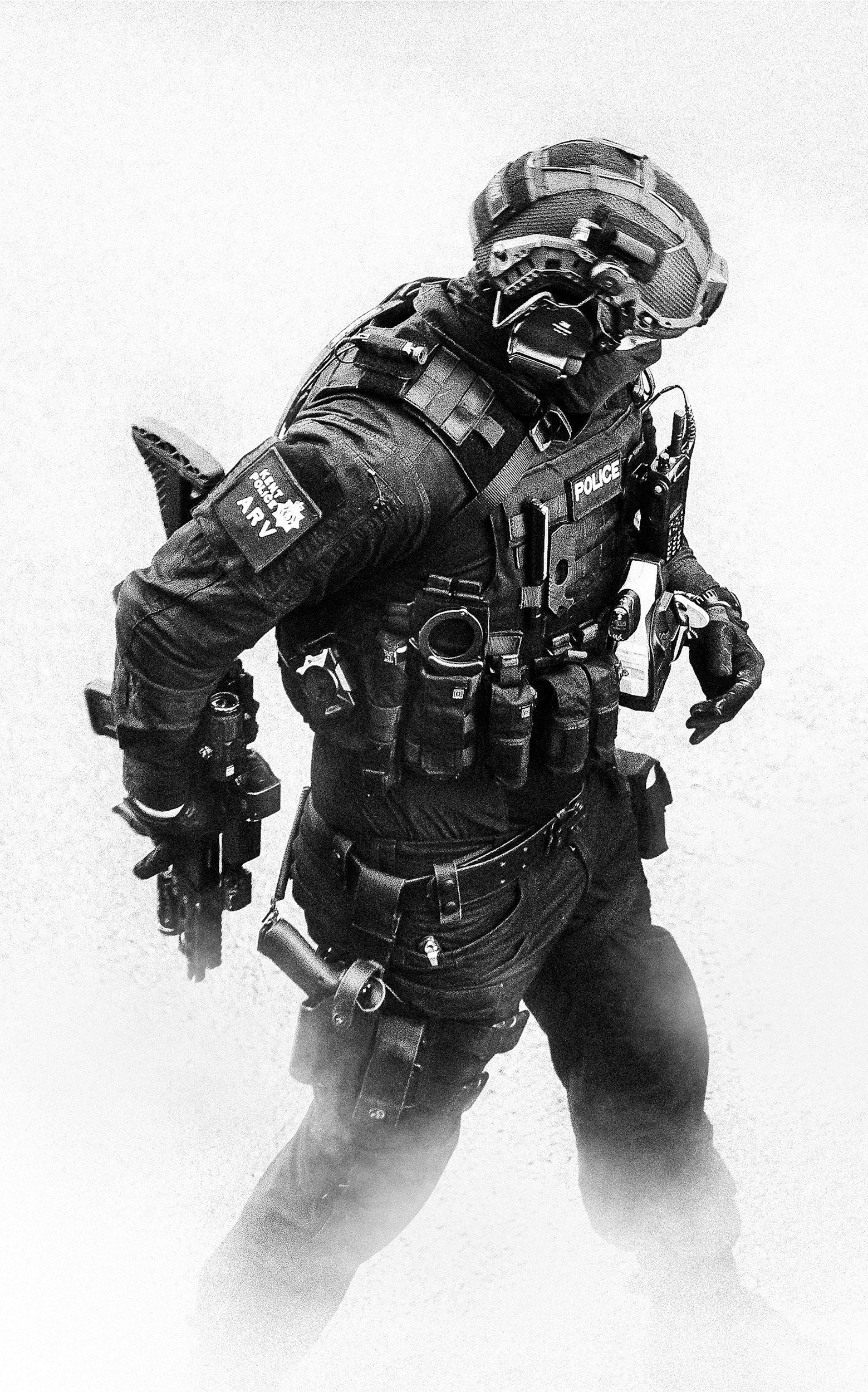 Black and white photo of a police officer in tactical gear, wearing a helmet and gloves, standing with one arm bent, holding a radio device in one hand, with various pouches and equipment attached to their vest.