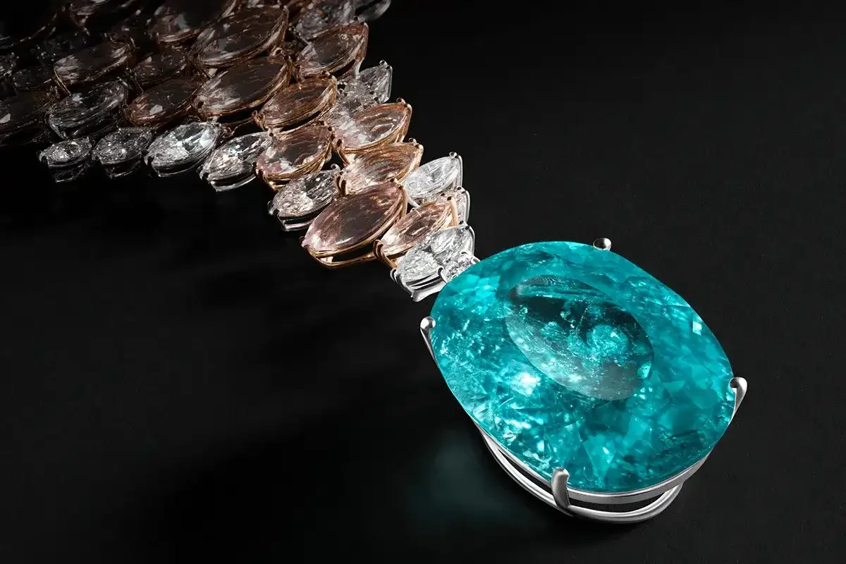 A necklace with a large, oval-shaped, blue gemstone pendant and multiple smaller, clear, and peach-colored gemstones on a black background.