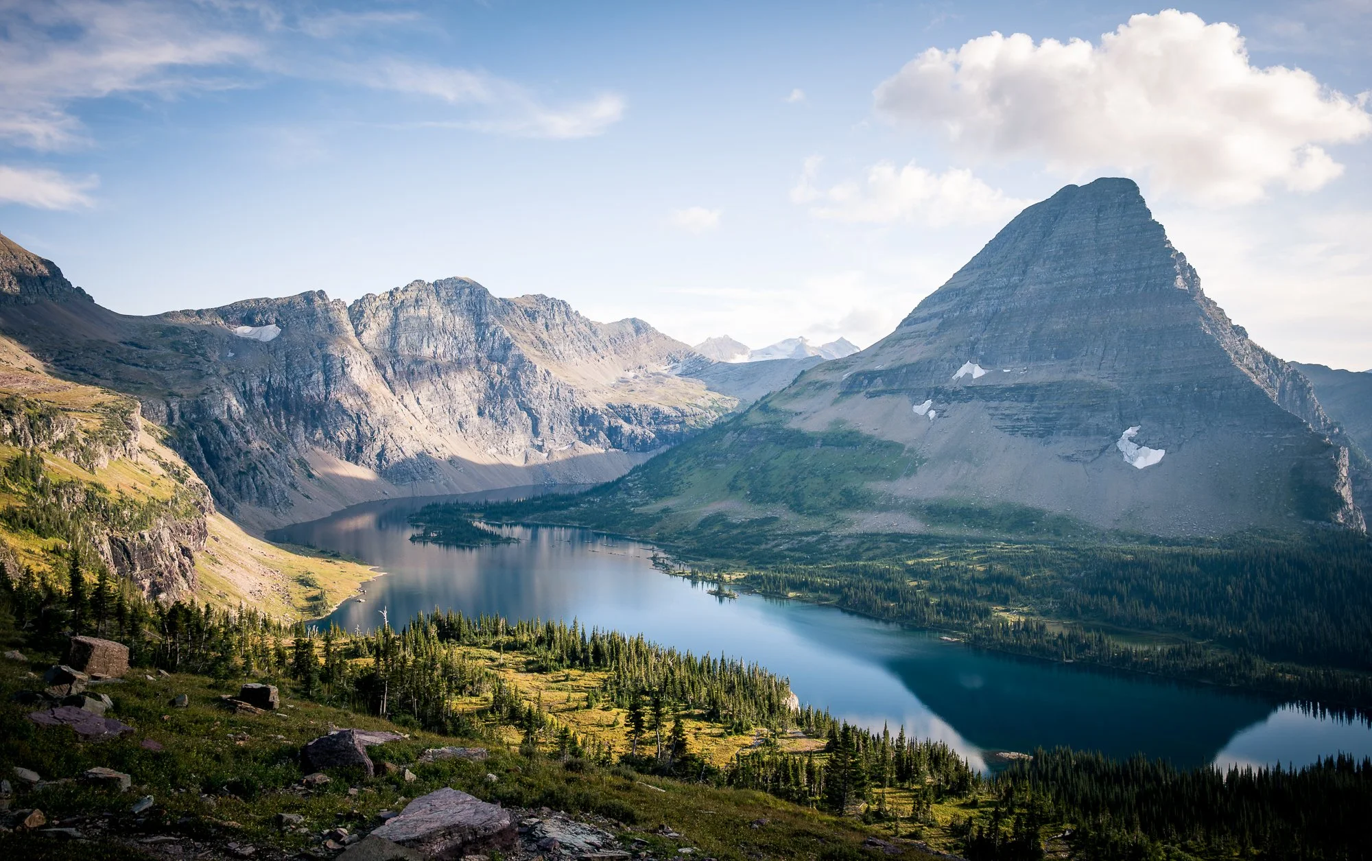 A mountain lake surrounded by steep rocky mountains and green forests under a partly cloudy sky.