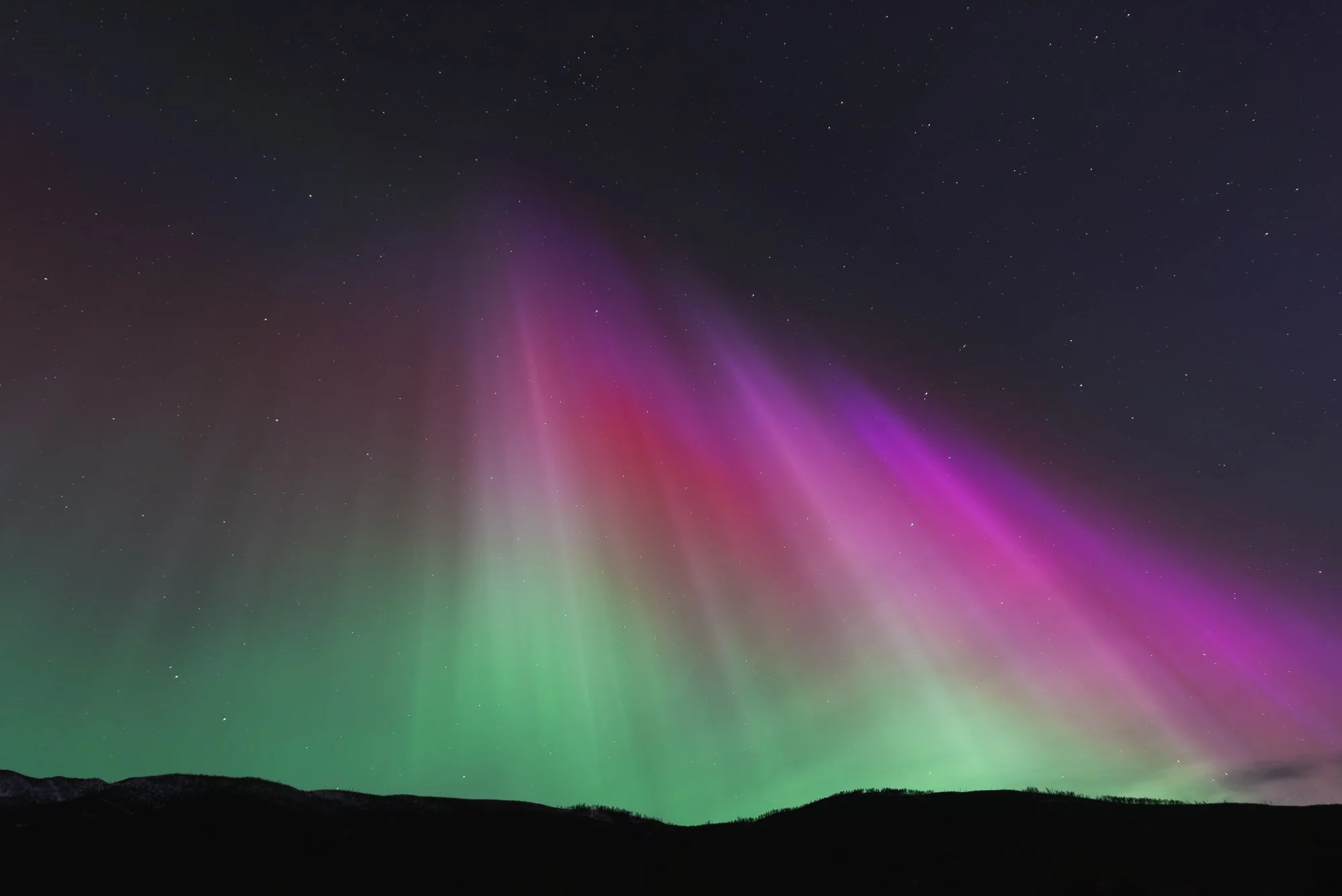Northern lights in a dark night sky with stars over a silhouette of a mountain range.