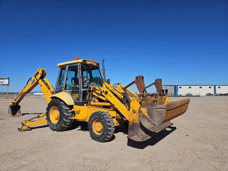 Yellow construction backhoe in an open dirt lot with a clear blue sky.