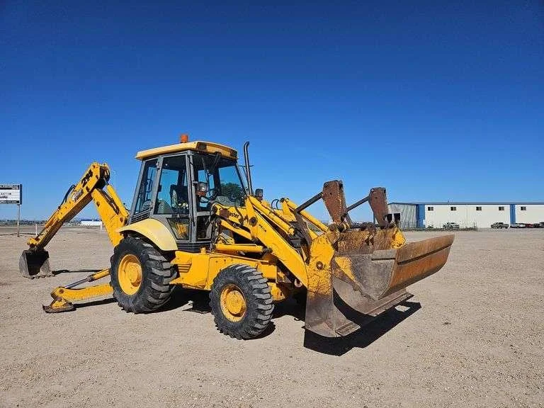 Yellow backhoe loader on a gravel lot with a blue sky.
