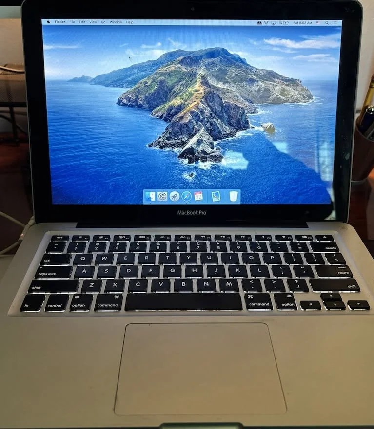 Close-up of a MacBook Pro laptop with the desktop background of a mountainous island surrounded by ocean.