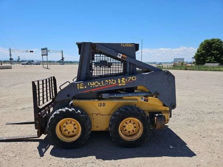 A yellow and black skid-steer loader with a bucket attachment, parked on a dirt lot under a blue sky.