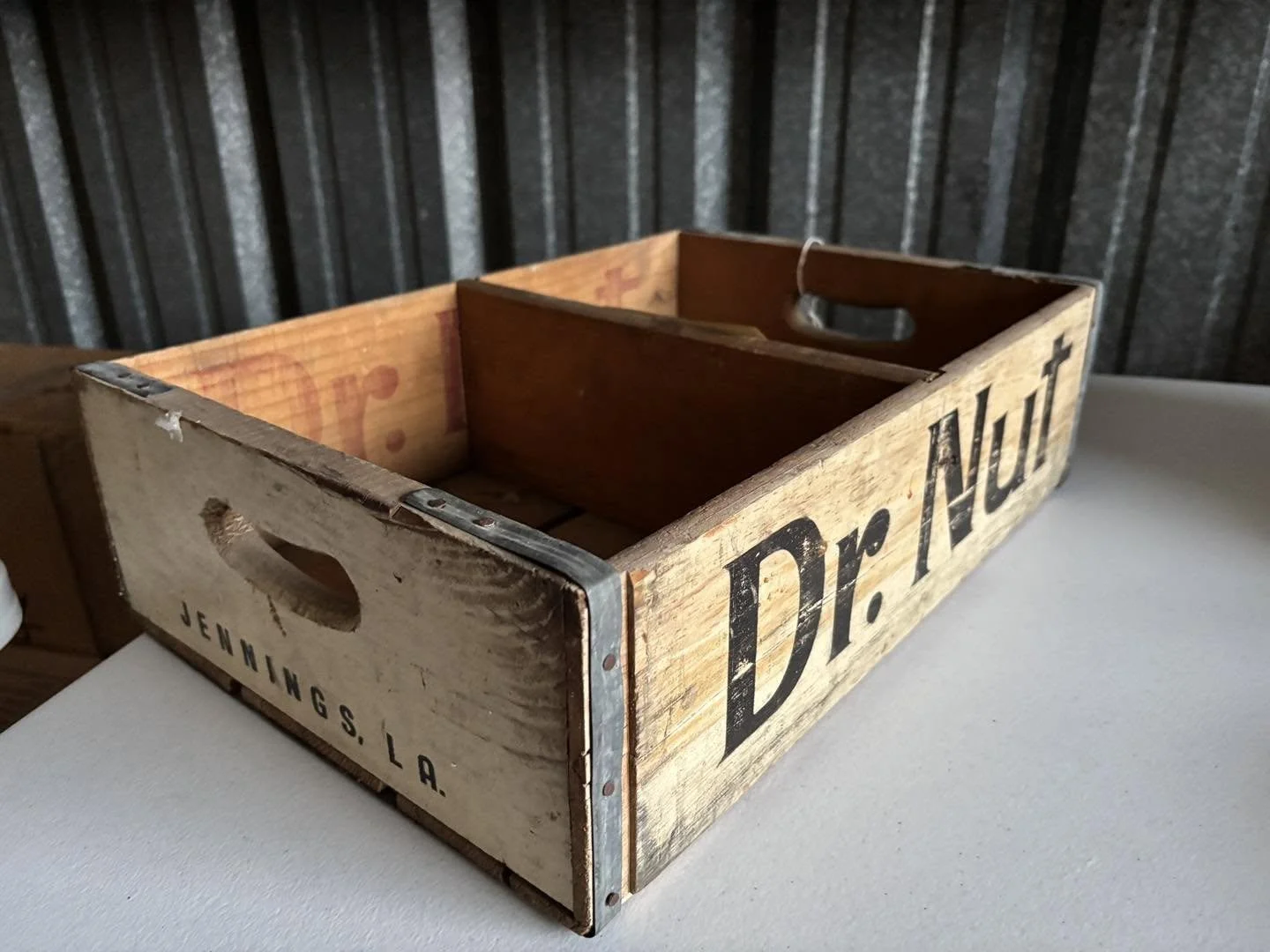 Wooden Dr. Nut crate with metal handle cutouts, labeled "Dr. Nut" and "Jennings, LA" on the side, on a white surface against a black vertical panel background.