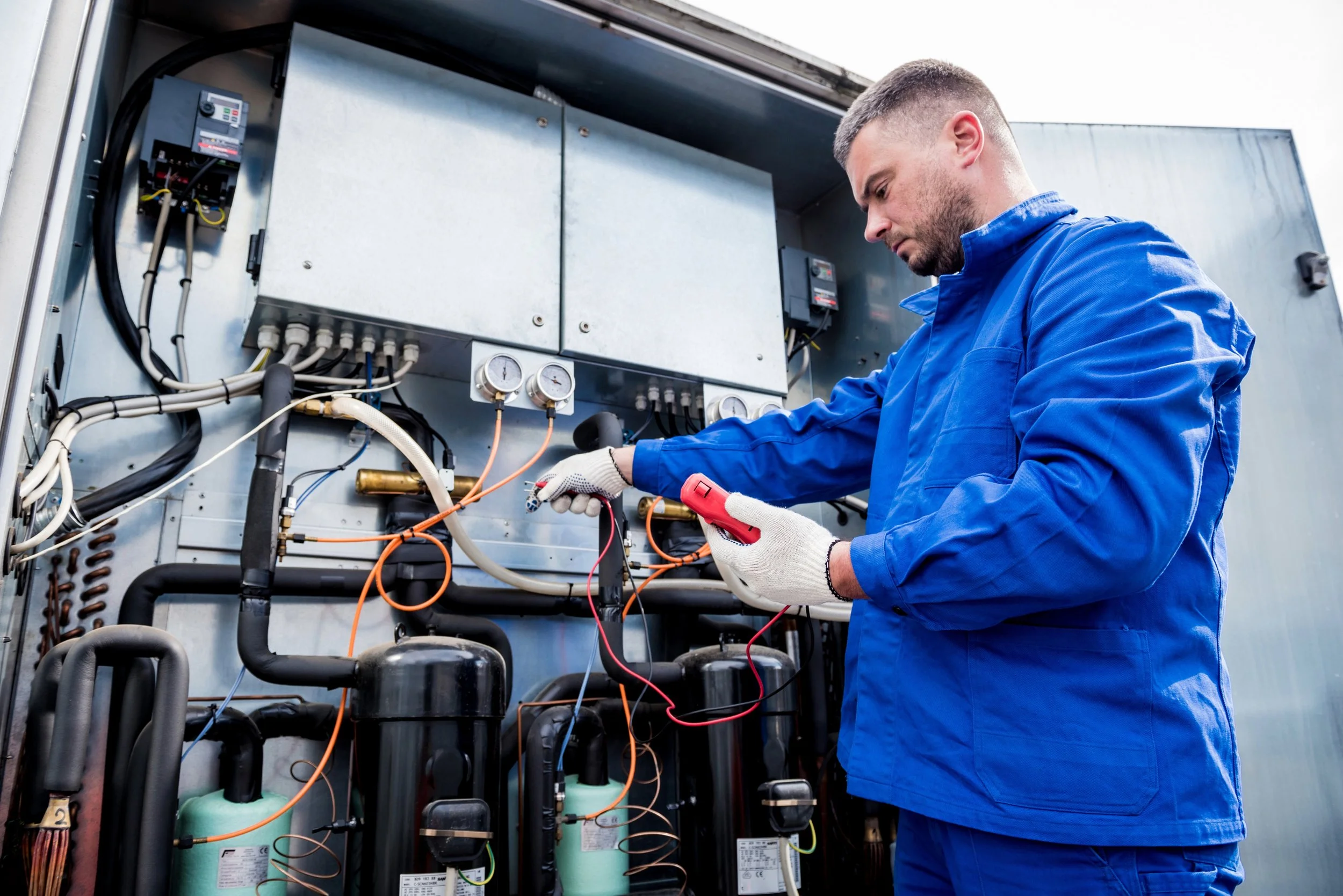 Technician inspecting HVAC equipment using a multimeter in an industrial setting.