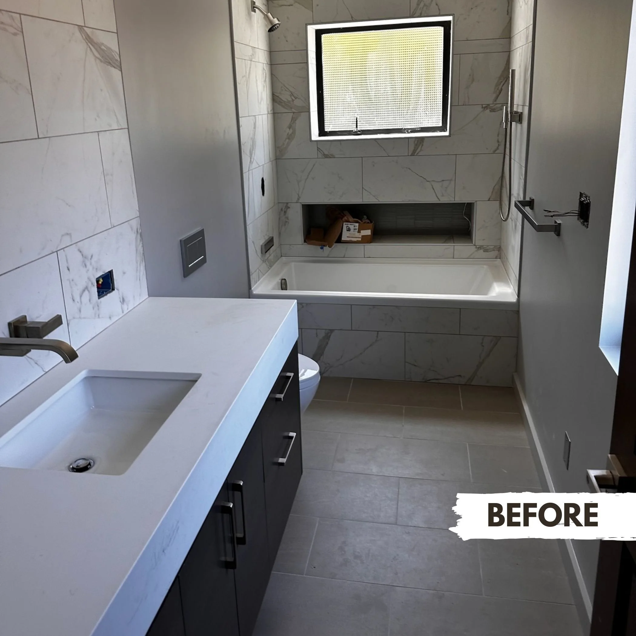 Bathroom with marble tile walls, a white bathtub, a small window, a white countertop with a built-in sink, and a dark vanity cabinet.