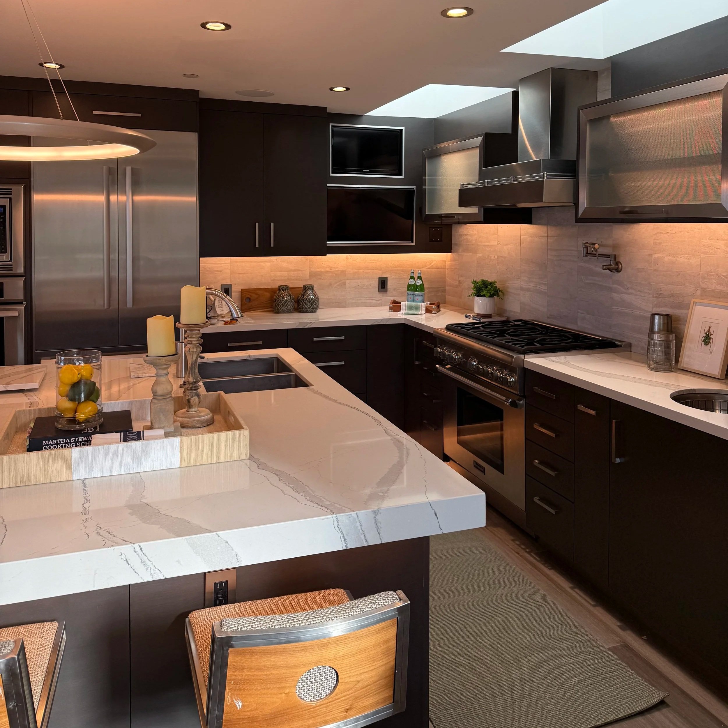 Modern kitchen with black cabinets, marble countertops, stainless steel appliances, and a kitchen island with decorative candles, books, and a tray of lemons and limes.