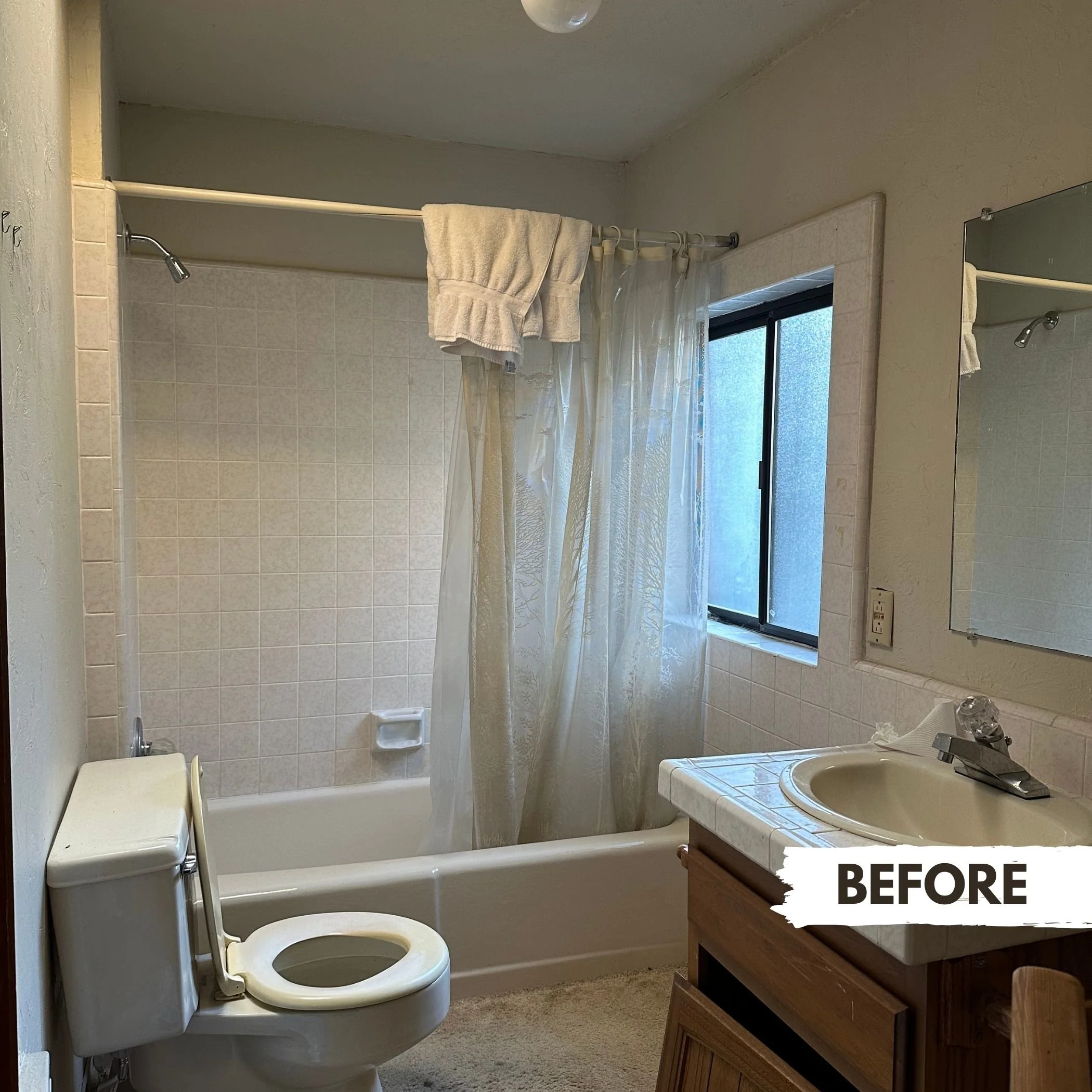 A small bathroom with a bathtub/shower combination, a toilet, a sink with a wooden vanity, a mirror, a frosted window, and a shower curtain. Towel hanging on the shower curtain rod.