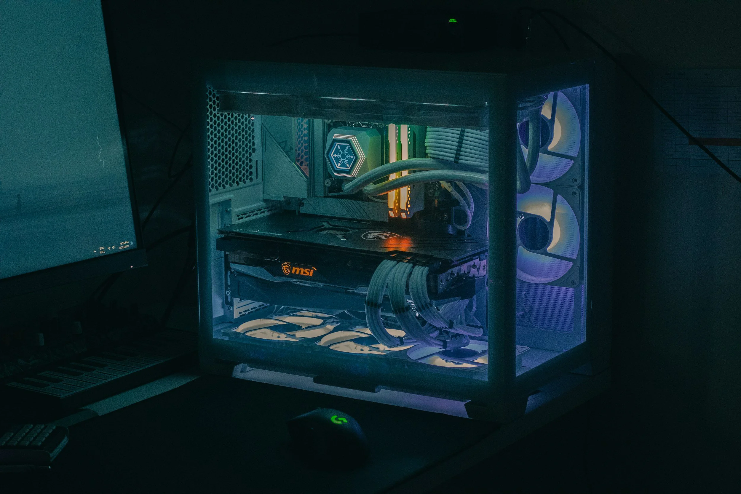 A gaming computer setup with a transparent side panel illuminated by RGB lighting, showing the intricate internal components like a graphics card, cooling fans, and wiring.