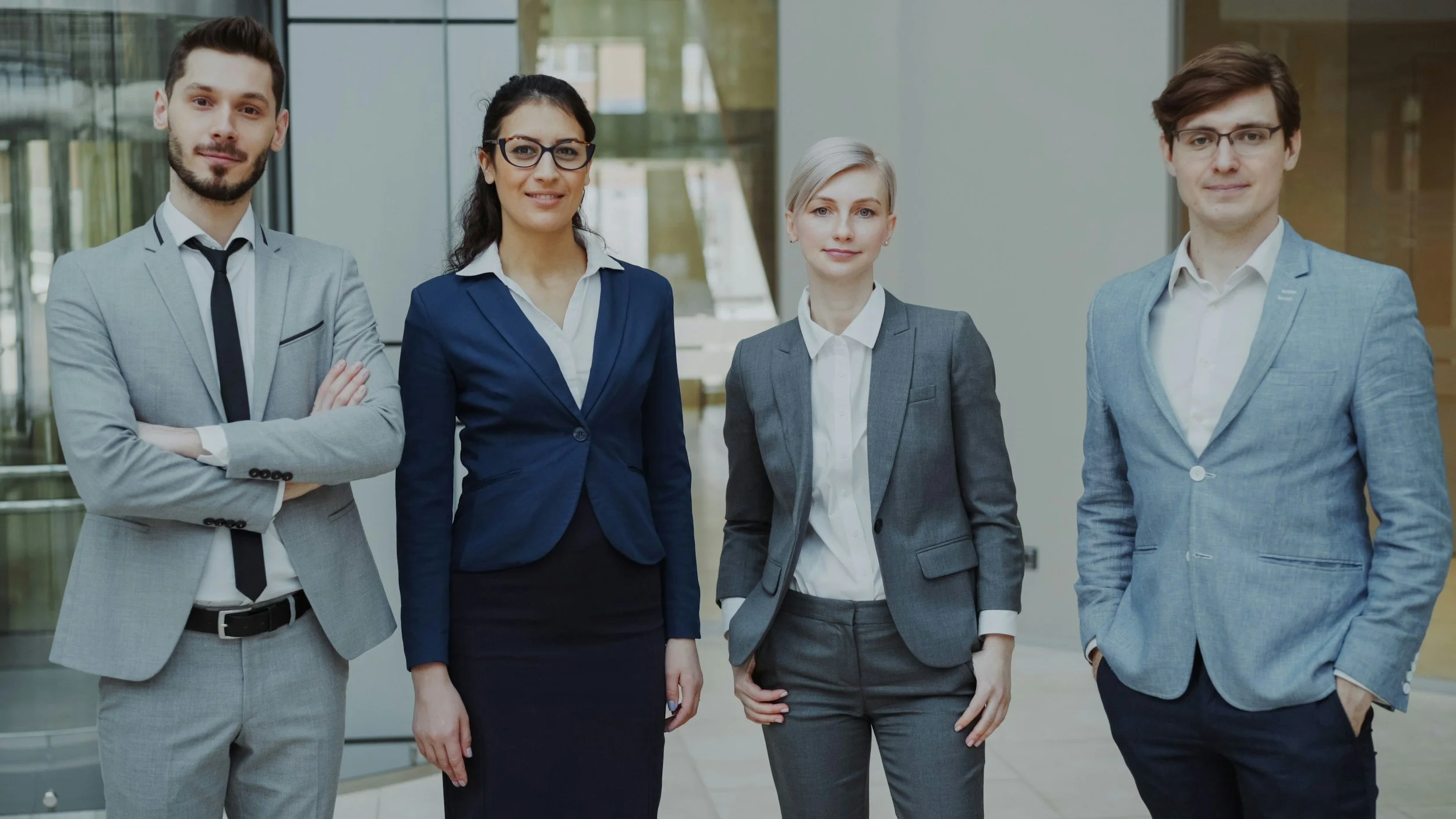 Four professionally dressed individuals standing in a modern office lobby, posing for a photo.