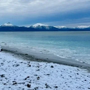 Snowy shoreline with mountains and cloudy sky in the background
