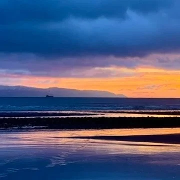 Sunset over a calm beach with dark clouds in the sky and reflections on the wet sand.