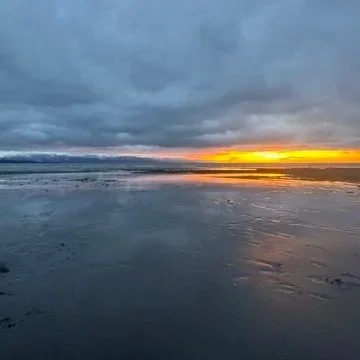 Sunset over a calm body of water with cloudy skies overhead.