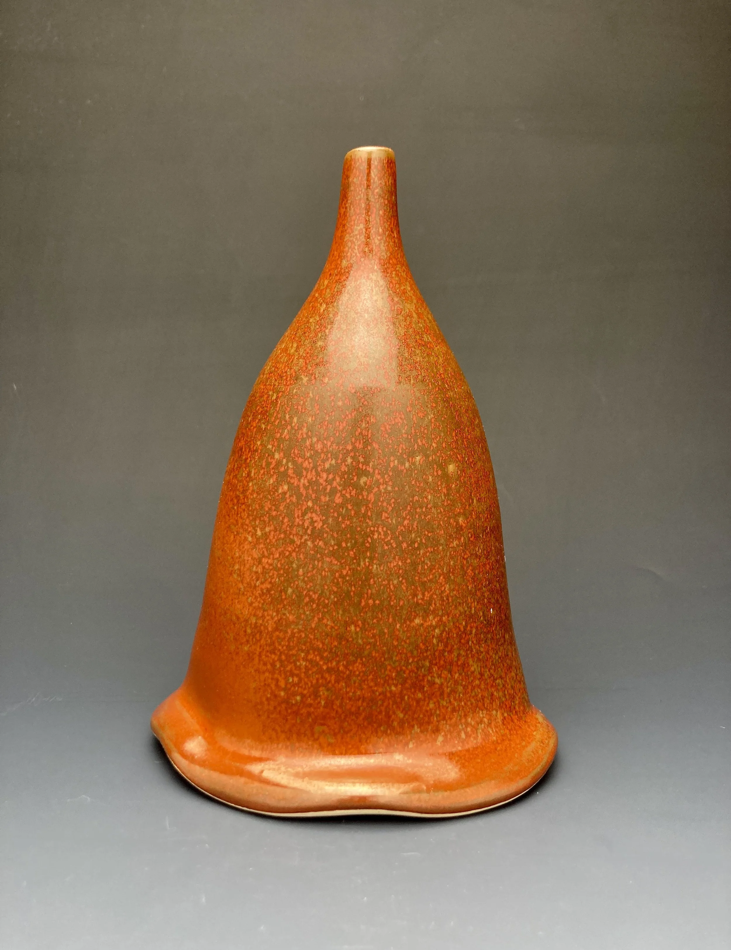 A mid-century modern orange ceramic vase with a textured surface, narrow neck, and flared base, set against a dark background. By Conner Burns.